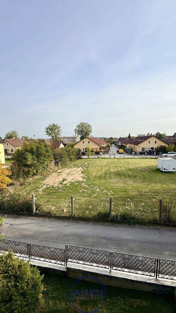 Blick auf eine ländliche Umgebung mit grünen Wiesen, einer Straße und Wohnhäusern in der Ferne.