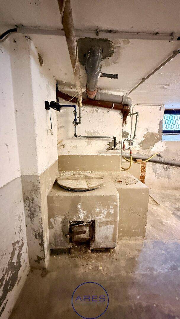 Unfertiger Kellerraum mit sichtbaren Rohren, Betonwänden und einer alten Heizungsanlage.