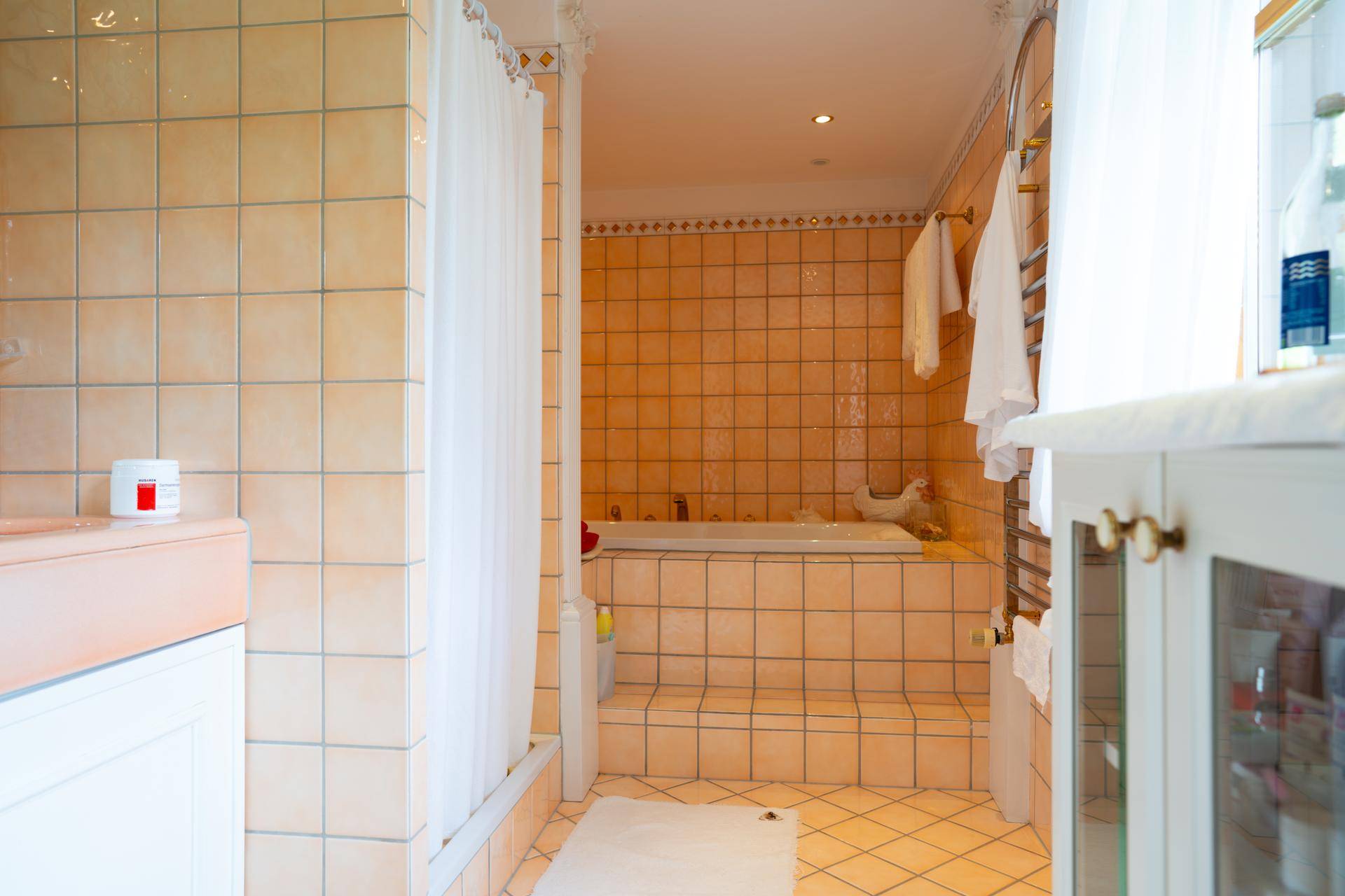 Helles Badezimmer mit Badewanne, Fliesen und beheiztem Handtuchhalter, in warmen Farbtönen.