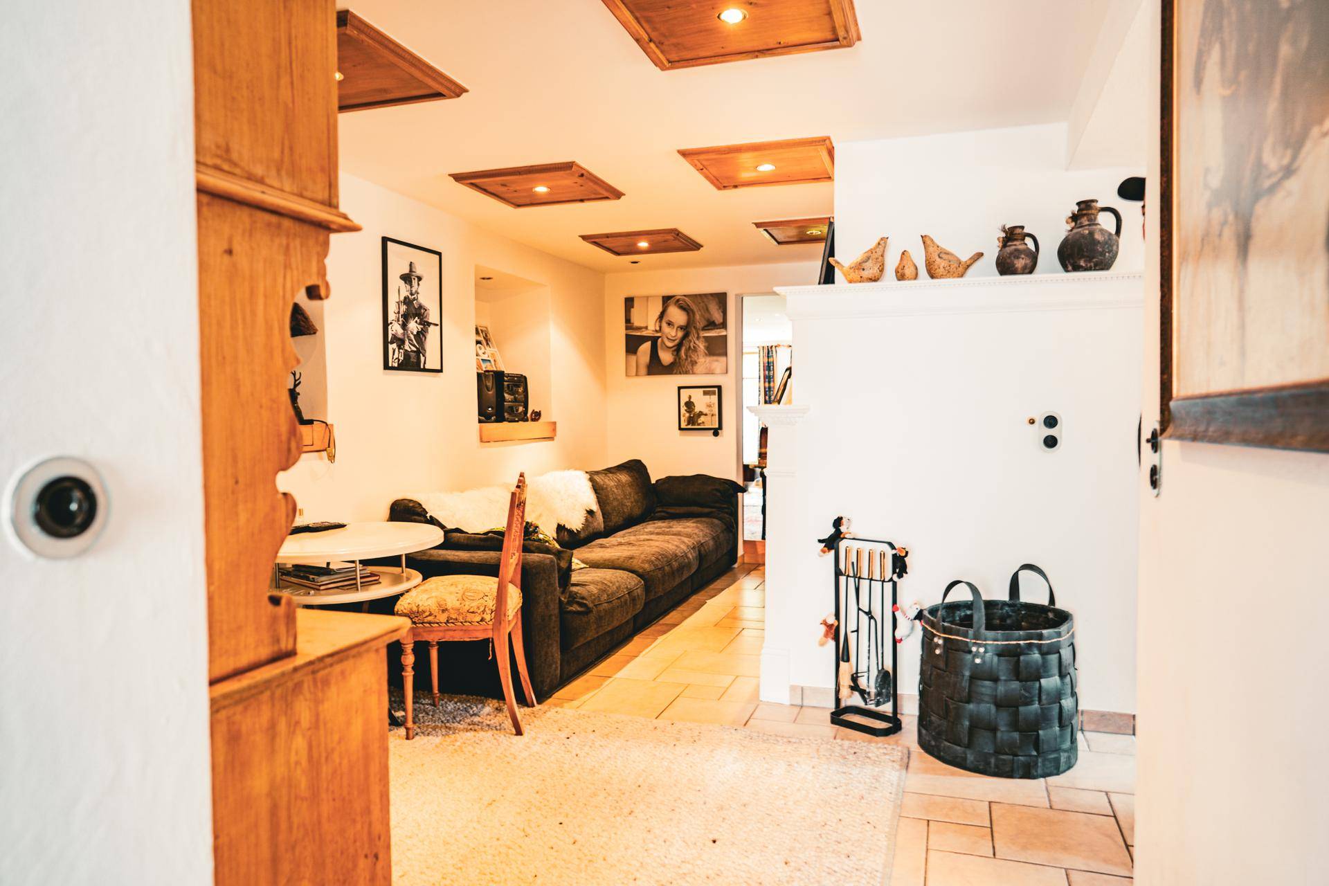 Gemütliches Wohnzimmer mit dunklem Sofa, Teppich und traditionellen Holzdeckenpaneelen.