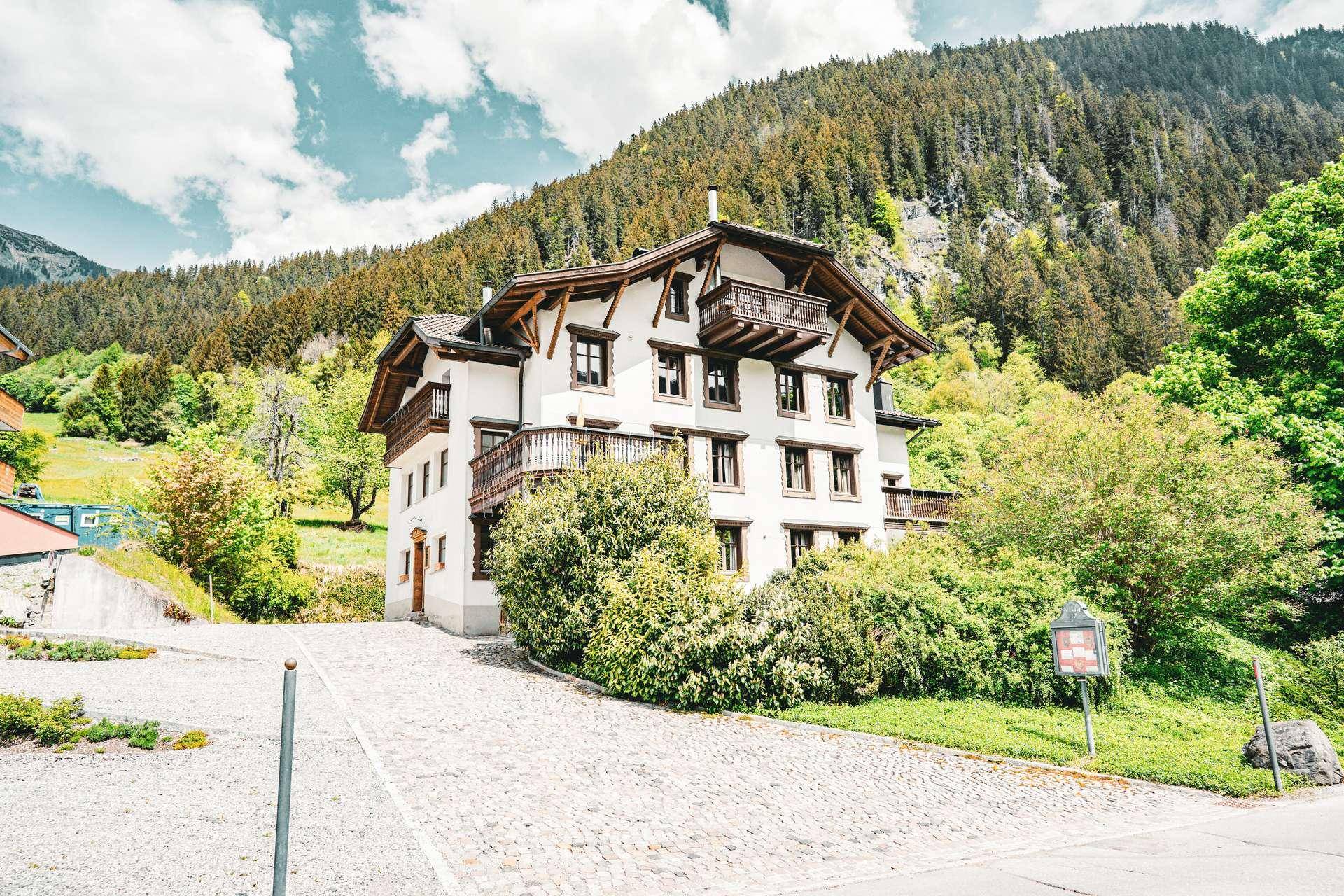 Charmantes Alpenhaus in den Bergen mit traditionellen Holzbalkonen und üppiger grüner Umgebung.
