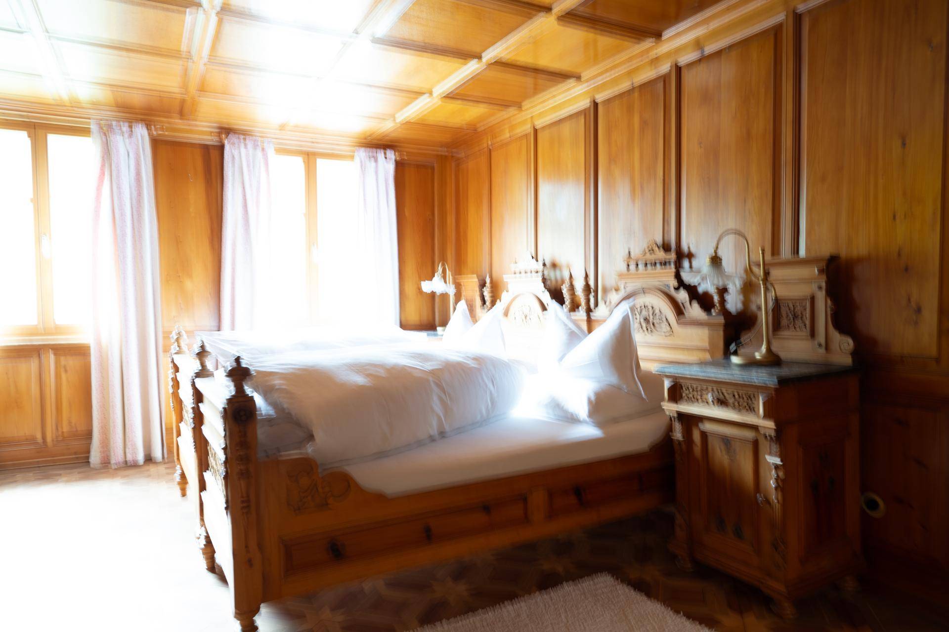 Traditionelles Schlafzimmer mit Holzbett, Holzvertäfelung und Kassettendecke, sehr hell.