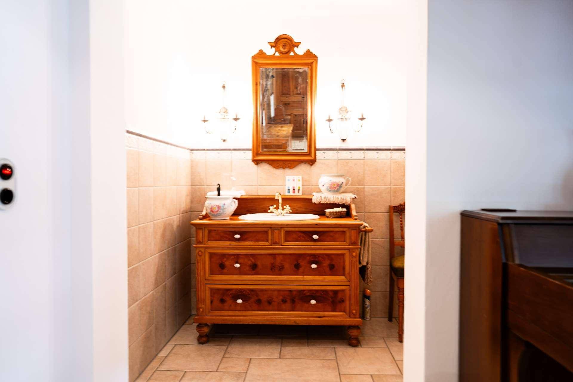 Badezimmer mit traditionellem Holzwaschtisch, Spiegel und Fliesenboden.
