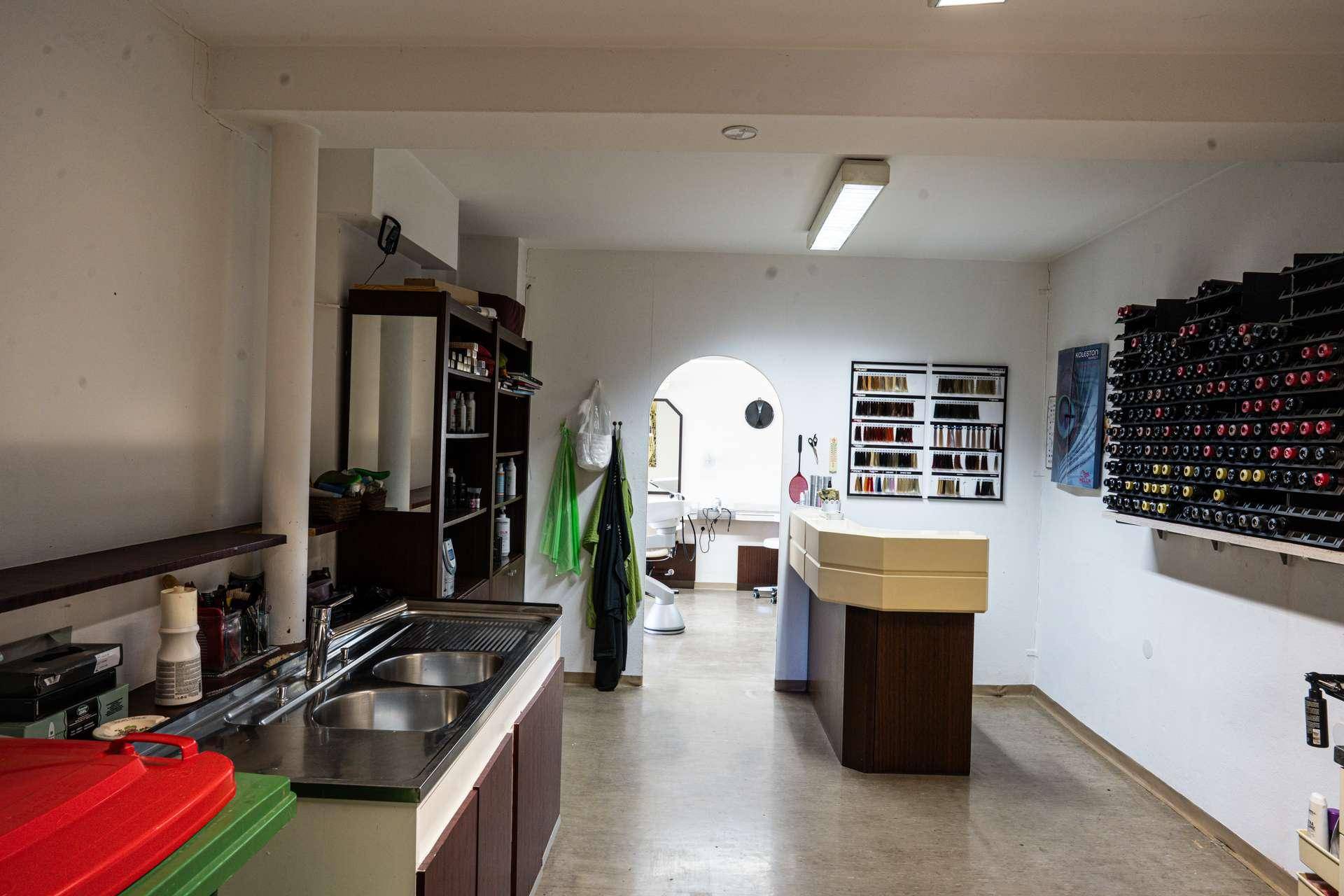 Hinterer Bereich eines Salons mit Waschbecken, Regalen und Produkten zur Haarpflege, funktional eingerichtet.