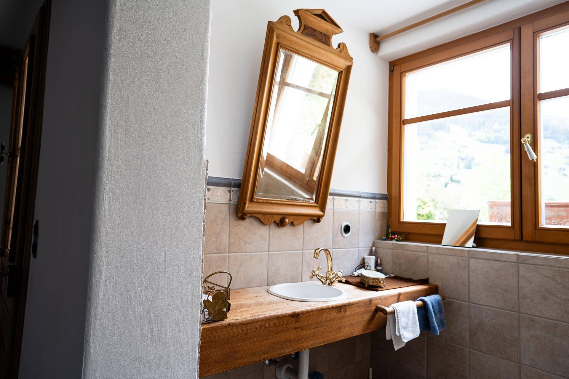 Traditionelles Badezimmer mit Holzwaschtisch, Spiegel und Fenster mit Bergblick.
