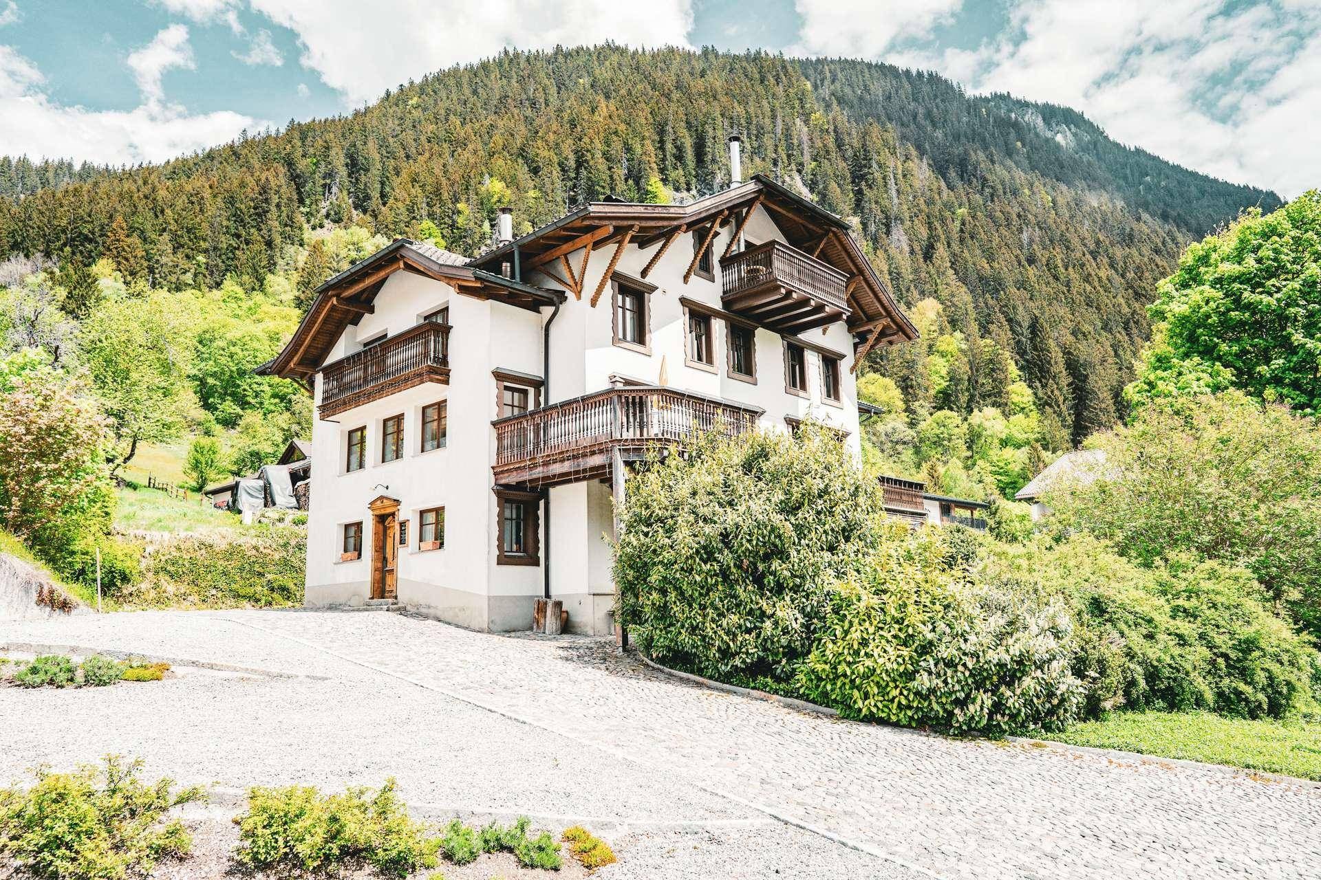 Charmantes Alpenhaus in den Bergen mit weißer Fassade und Holzelementen unter blauem Himmel.