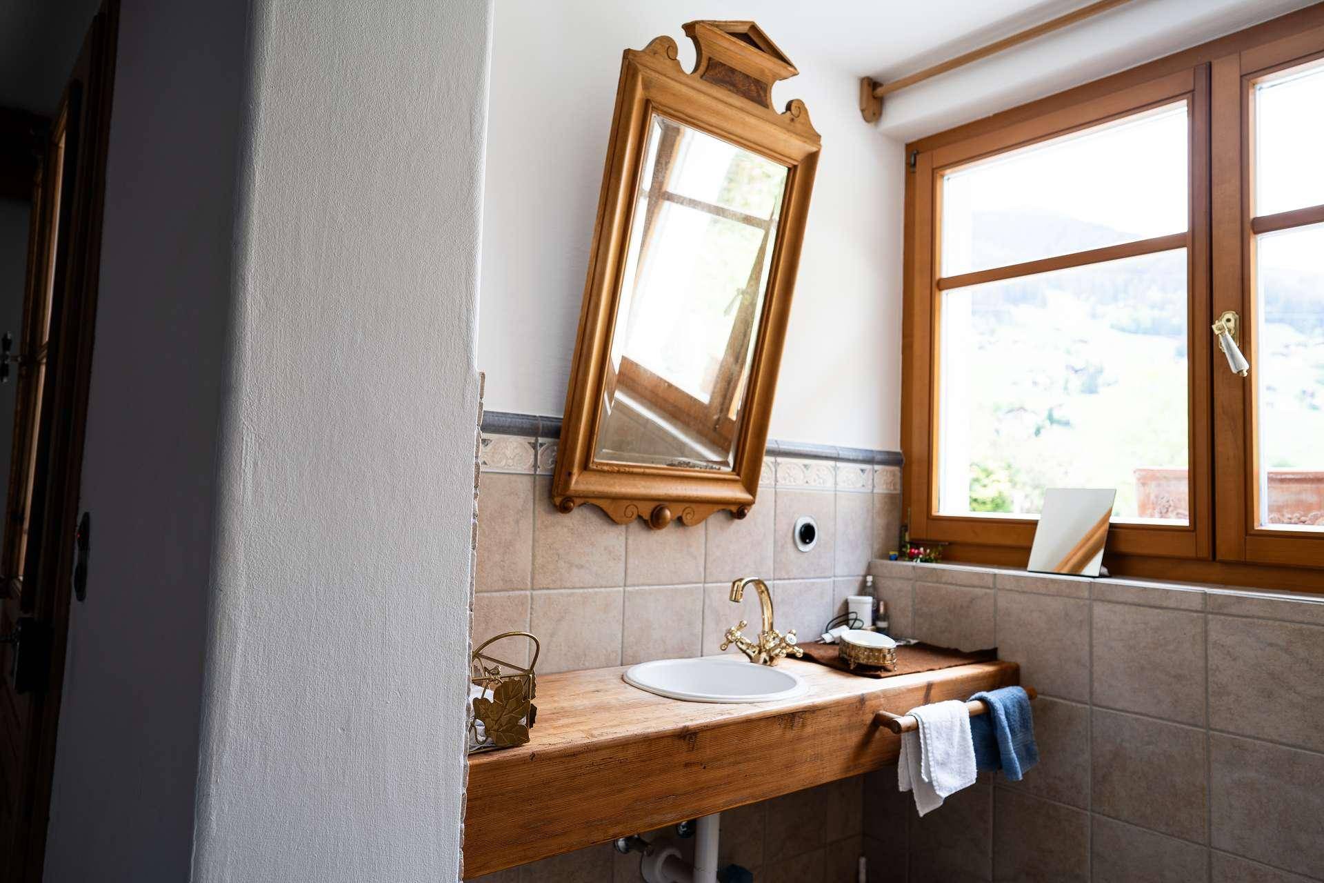 Helles Badezimmer mit Holzwaschtisch, Spiegel und Fenster mit Bergblick.