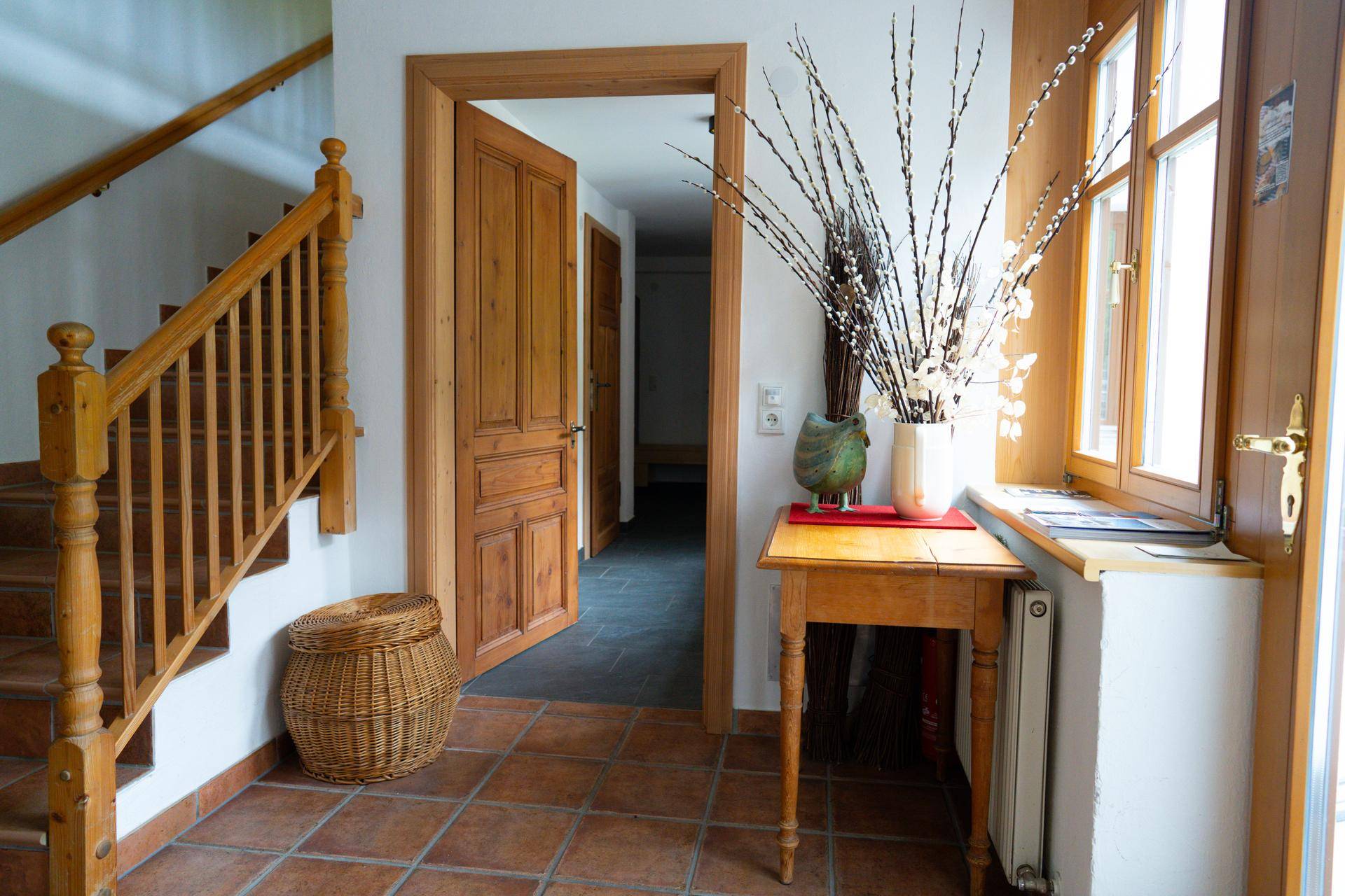 Heller Eingangsbereich mit Holztreppe, Terrakottafliesen und einem dekorativen Beistelltisch.