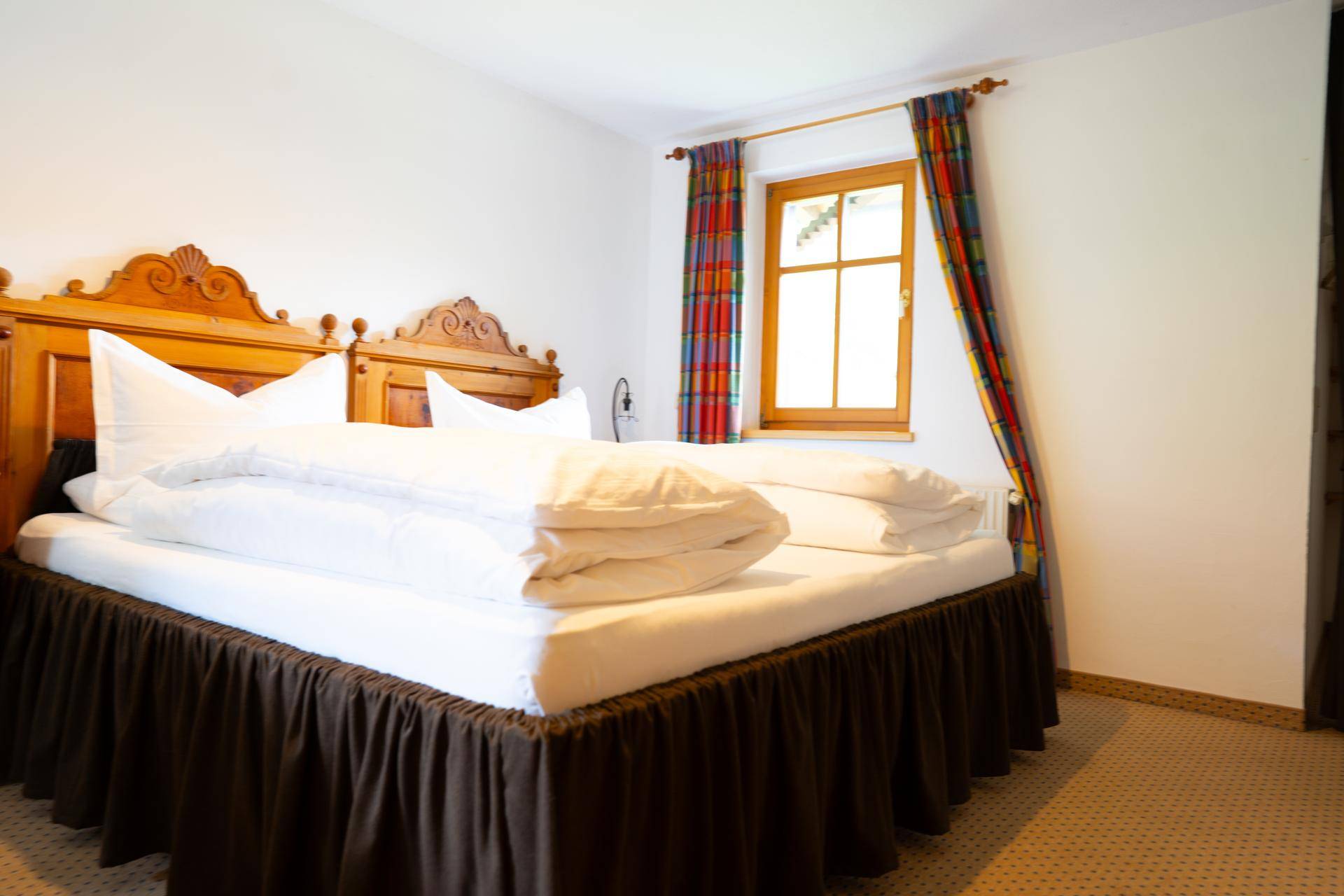Gemütliches Schlafzimmer mit Doppelbett, Teppichboden und bunten Vorhängen.