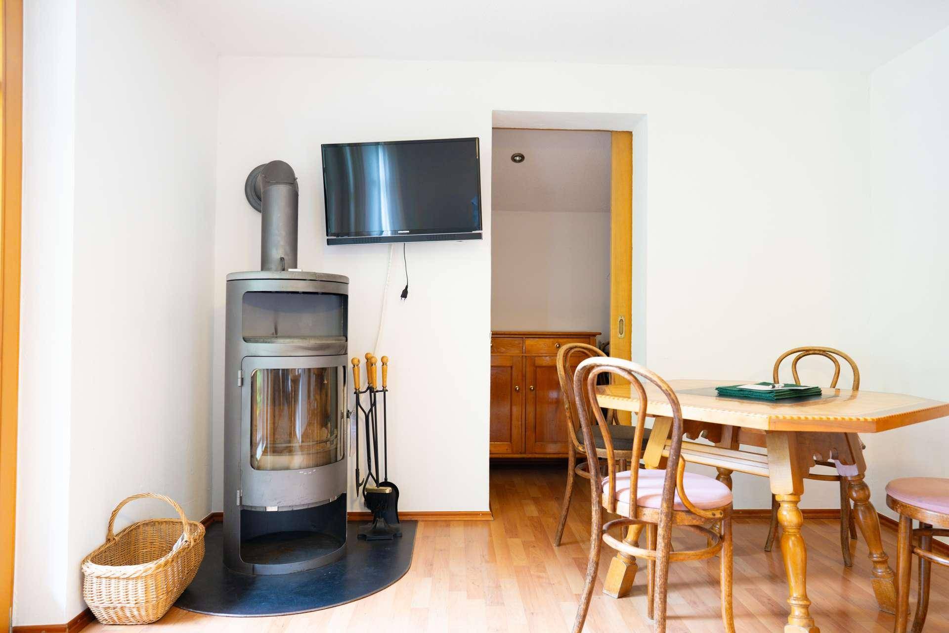 Wohnbereich mit modernem Holzofen, Esstisch und Fernseher an der Wand.