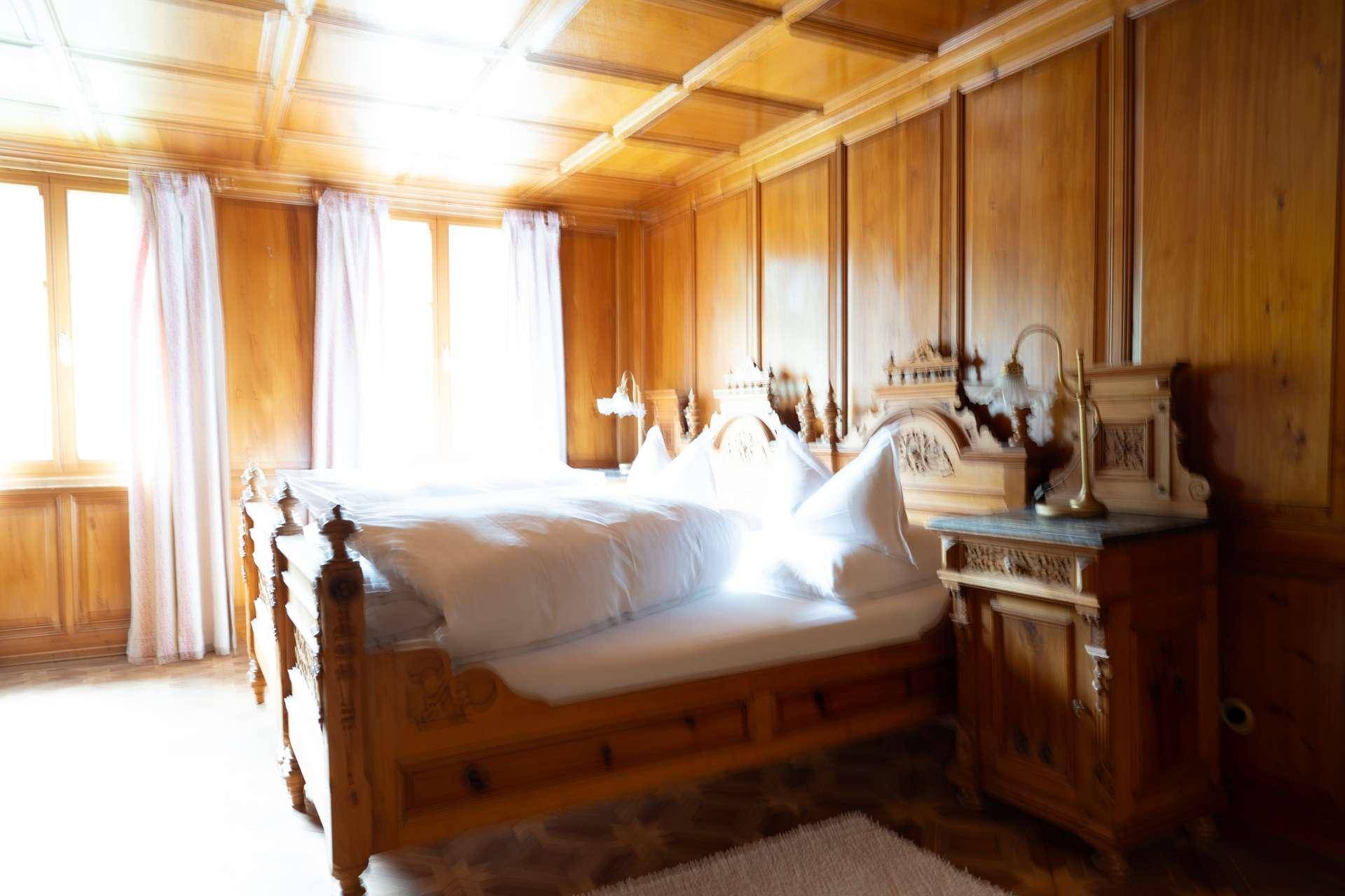 Helles Schlafzimmer mit Holzboden, Holzdecke und traditionellem Holzbett.