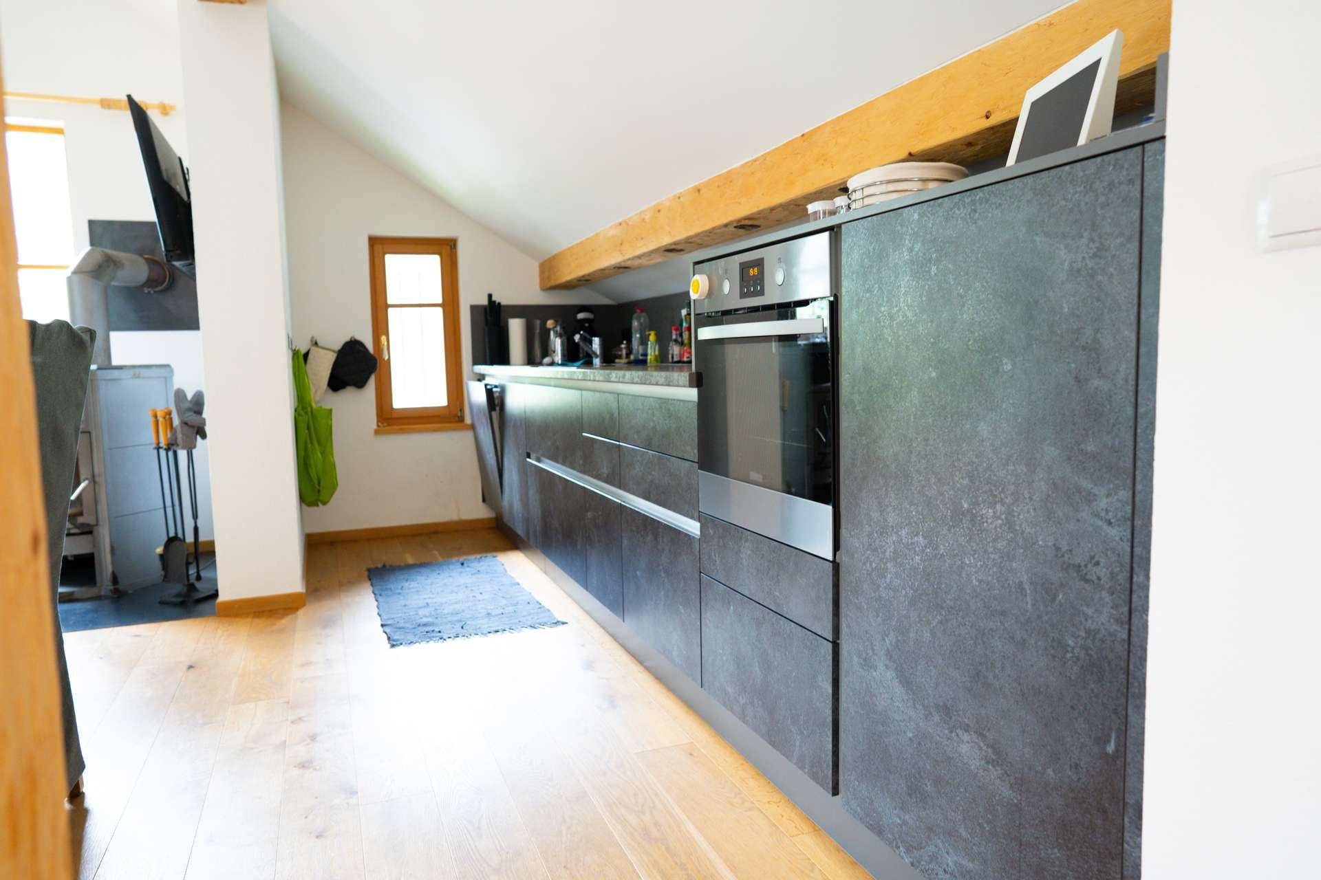 Moderne Küche im Dachgeschoss mit dunklen Schränken, Holzbalken und Holzboden.