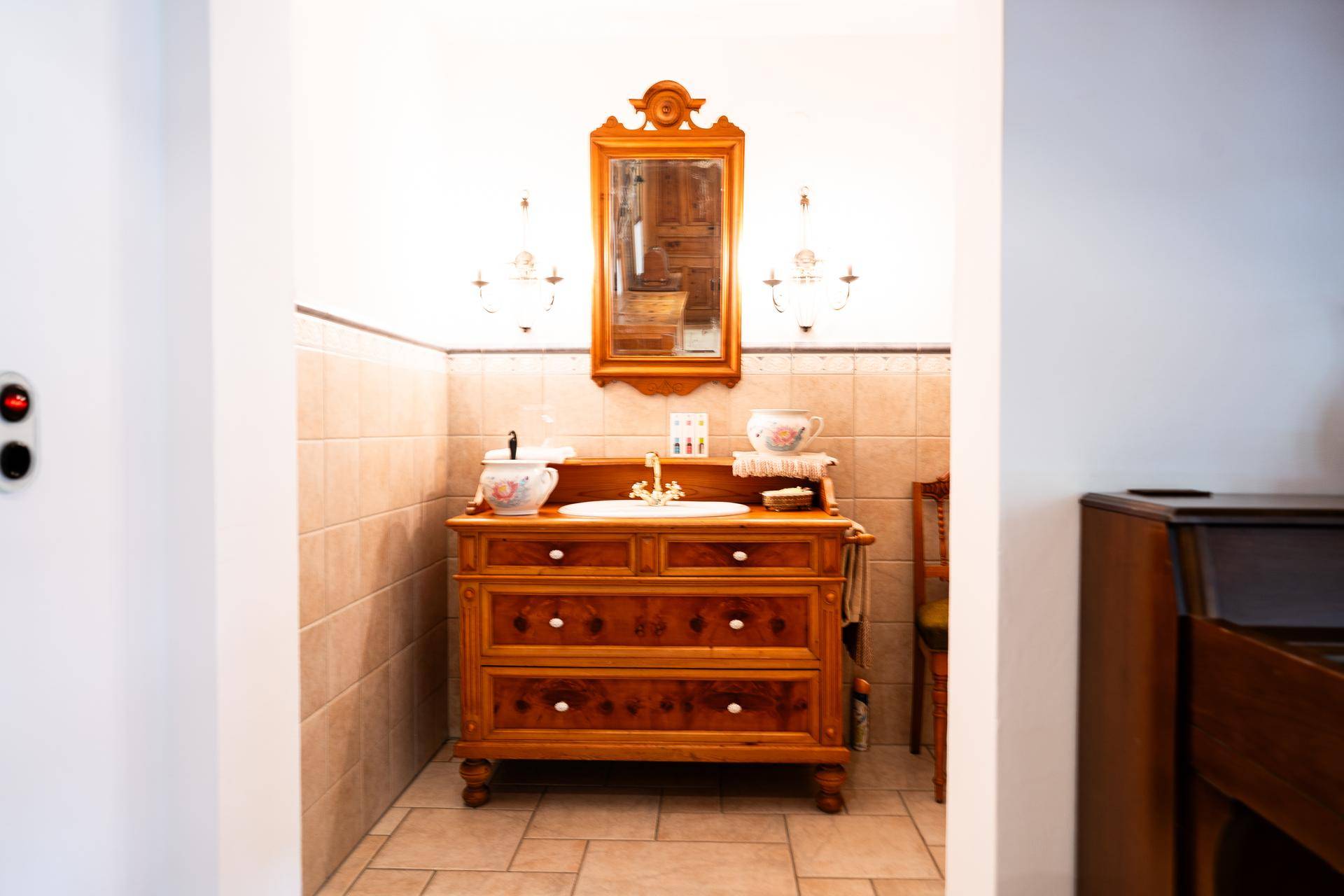 Charmantes Badezimmer mit antikem Waschtisch, Spiegel und Wandleuchten im traditionellen Stil.