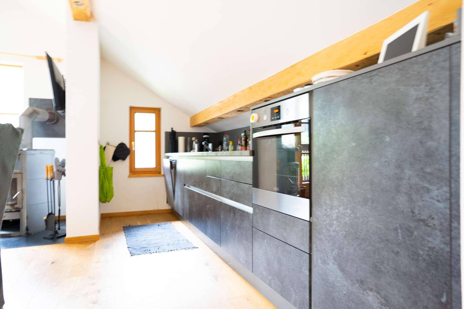 Moderne Küche mit grauen Fronten, Holzbalken und integrierten Geräten unter Dachschräge.