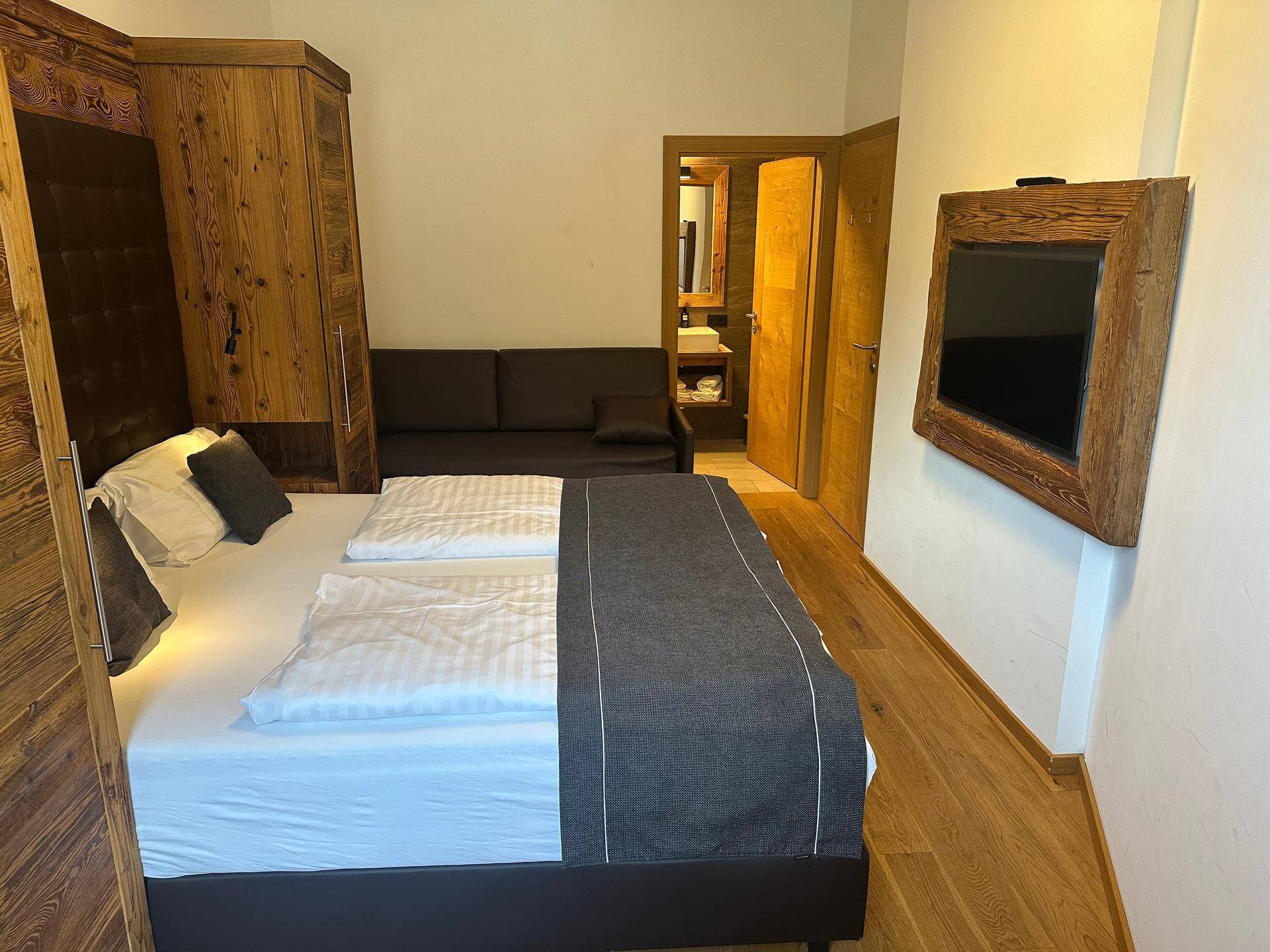 Komfortables Schlafzimmer mit Doppelbett, Sofa und einem Fernseher, mit Zugang zum Badezimmer.