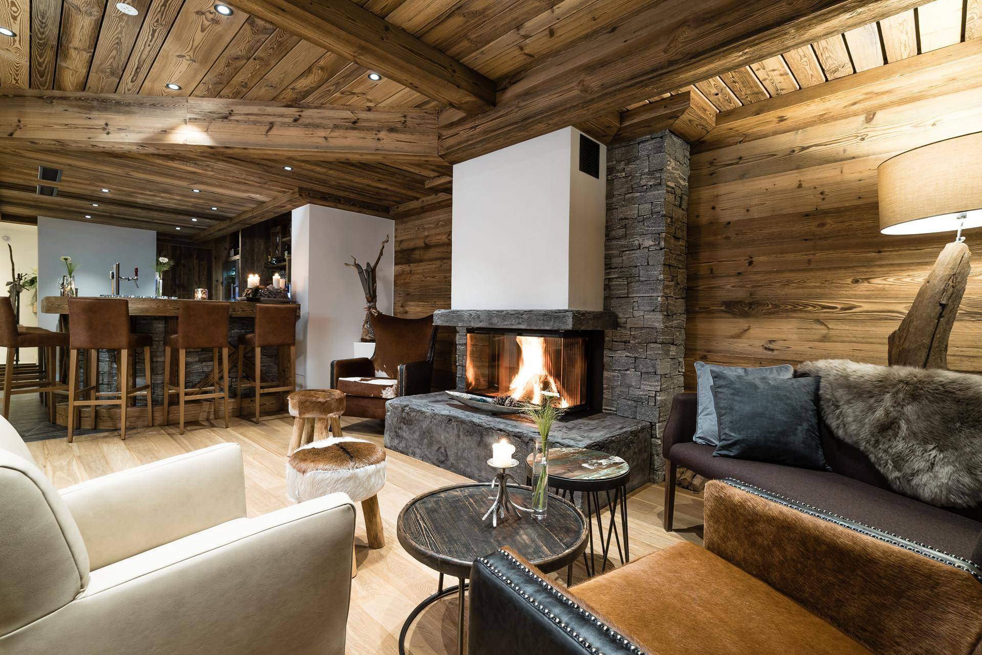 Gemütliches Wohnzimmer im alpinen Stil mit Holzbalken, Kamin und einer integrierten Bar.
