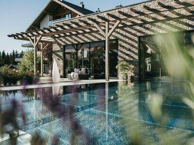 Großer Außenpool mit Holzpergola und moderner Gebäudefassade unter blauem Himmel.