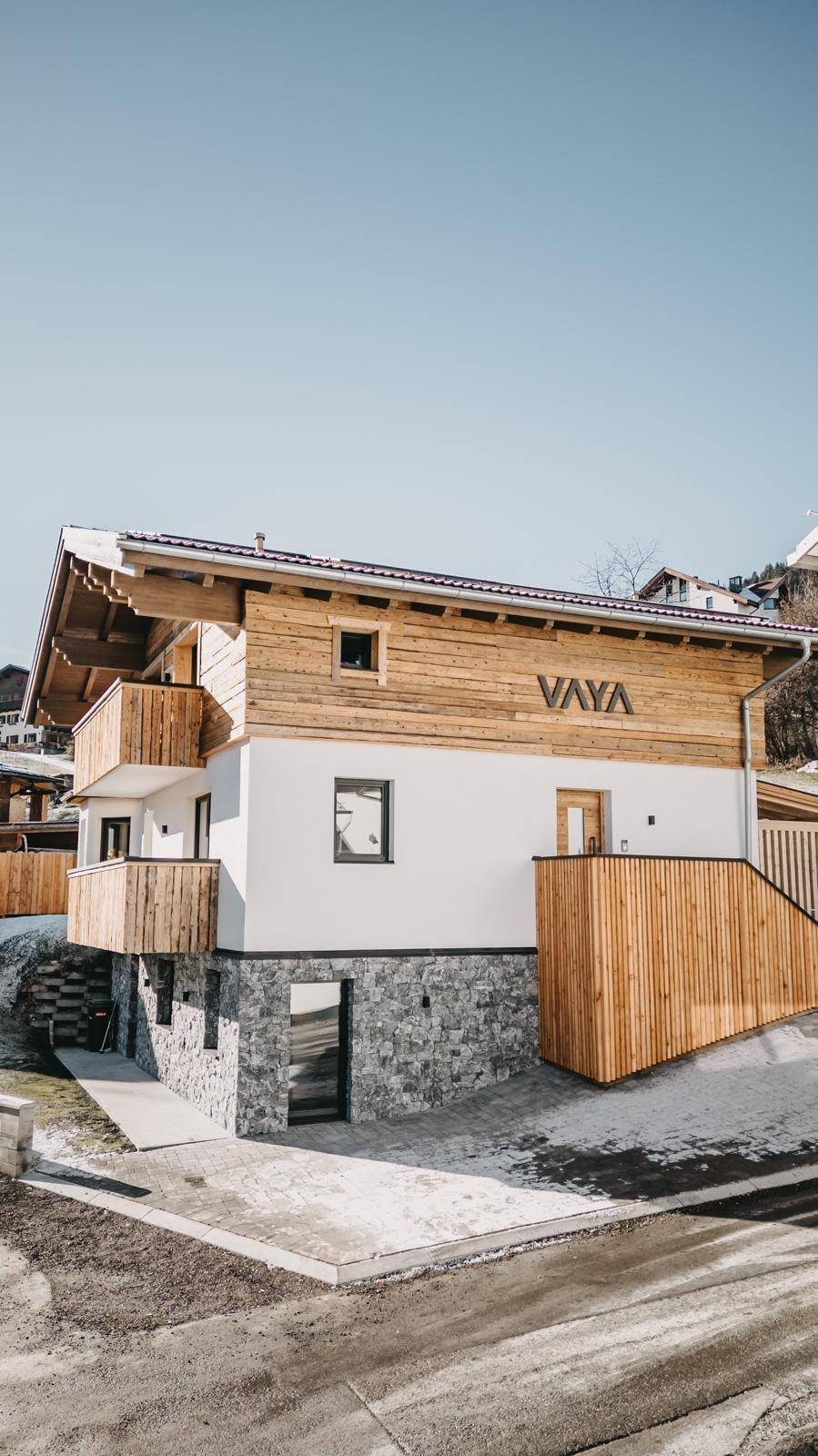 Ansicht des modernen Gebäudes mit Holzverkleidung, weißer Fassade und Steinsockel unter blauem Himmel.