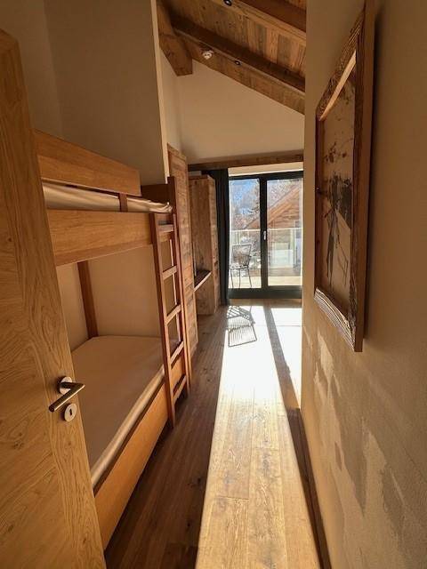 Helles Schlafzimmer mit Etagenbetten, Holzboden und Zugang zu einem Balkon.