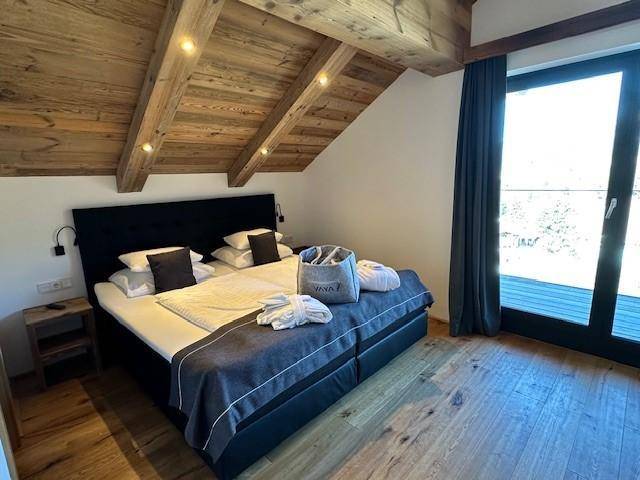 Helles Schlafzimmer mit Doppelbett, Holzbalkendecke und großen Fenstern.