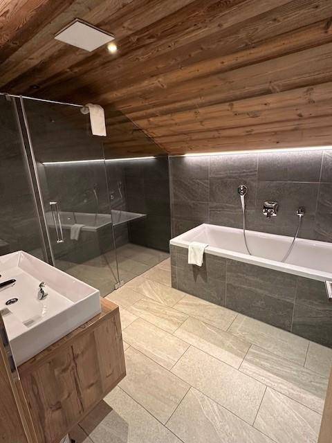 Modernes Badezimmer mit Badewanne, begehbarer Dusche und Doppelwaschbecken unter Holzbalkendecke.