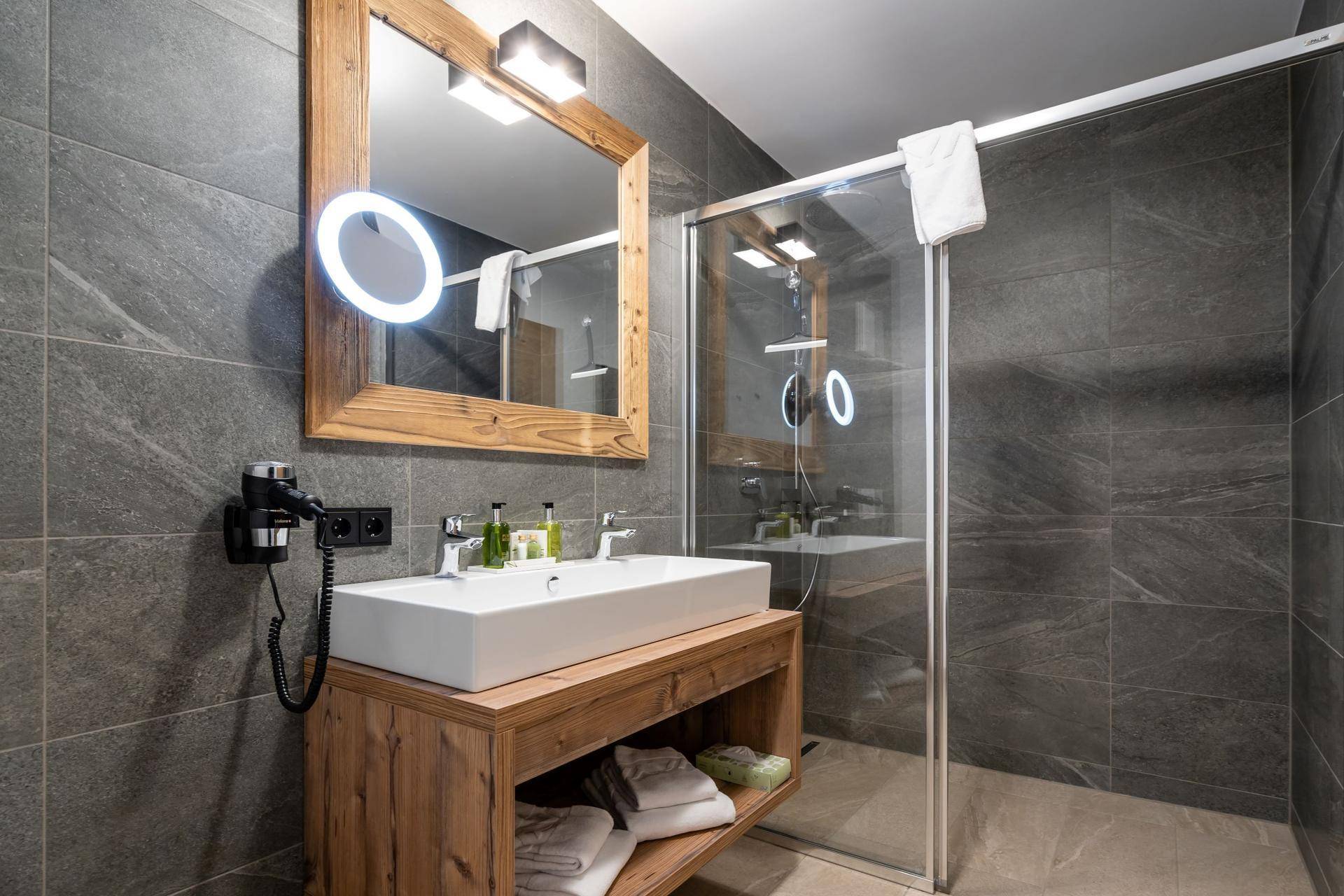 Modernes Badezimmer mit großer Dusche, Holzwaschtisch und dunklen Fliesen.