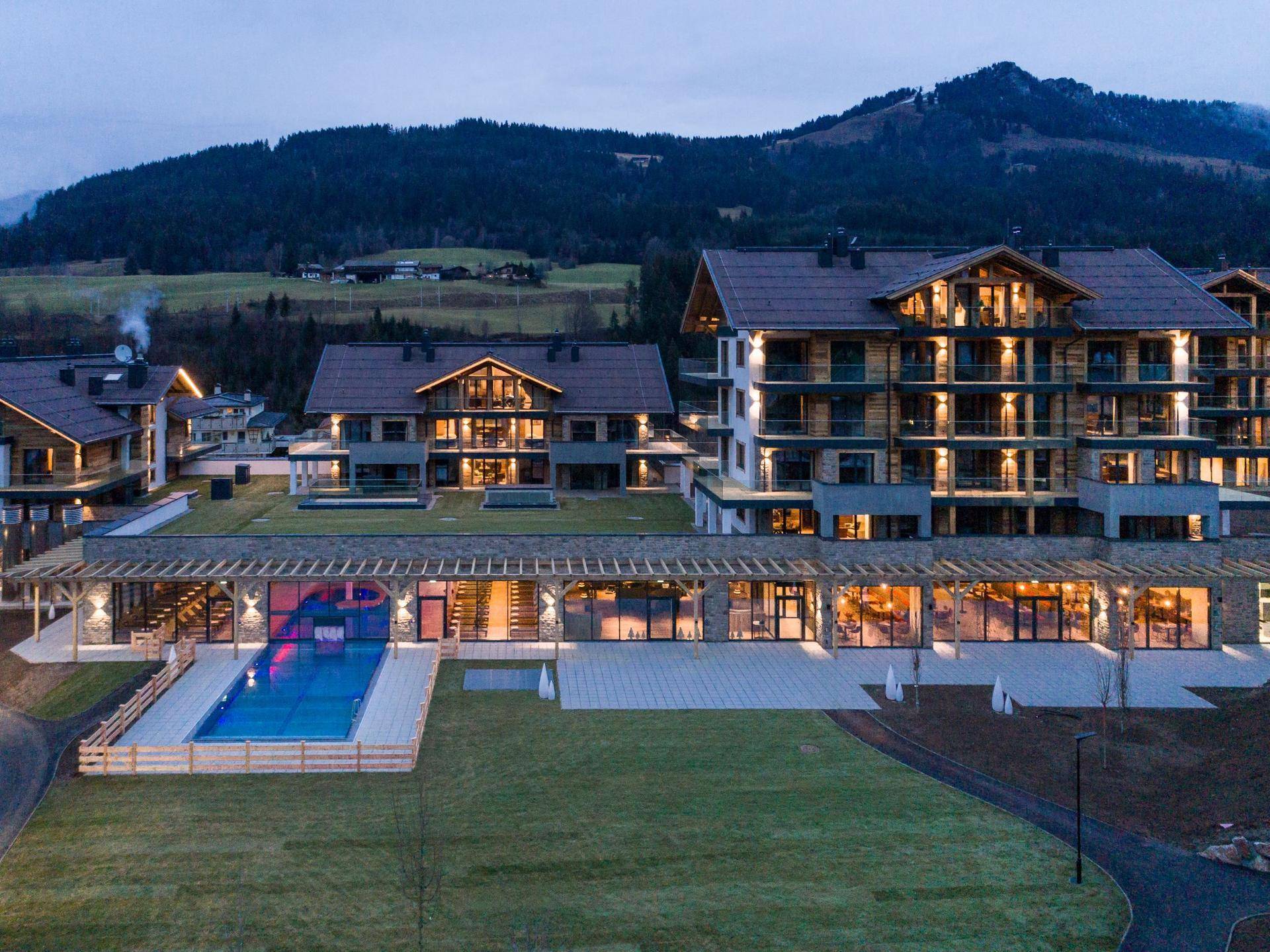 Resortanlage mit Außenpool, weitläufigen Grünflächen und Bergblick bei Abenddämmerung.