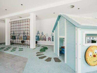 Farbenfroher Kinderspielbereich mit Spielhaus, Kletternetz und kreativer Wandgestaltung.