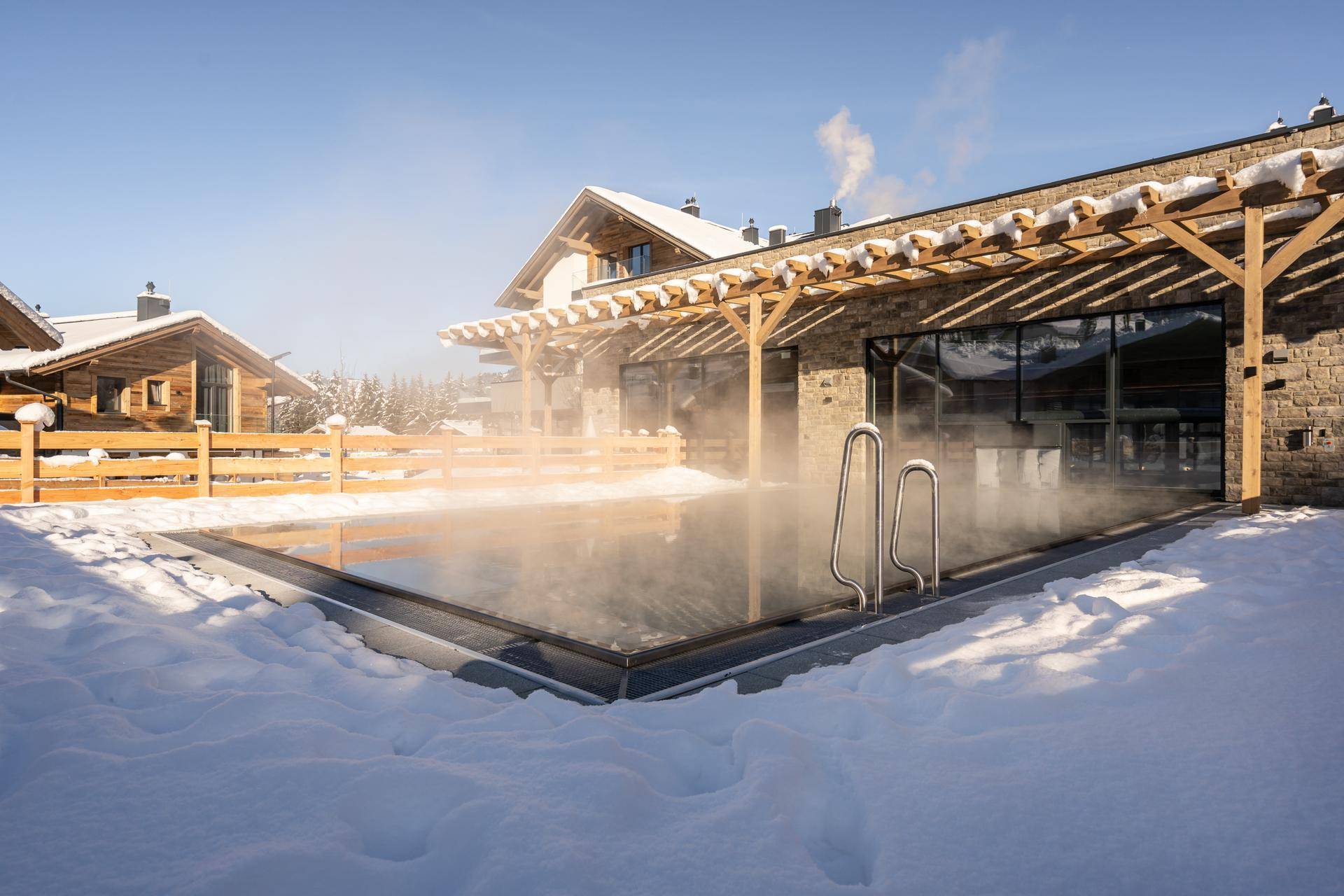 Beheizter Außenpool im Schnee mit umliegenden Gebäuden und winterlicher Berglandschaft.