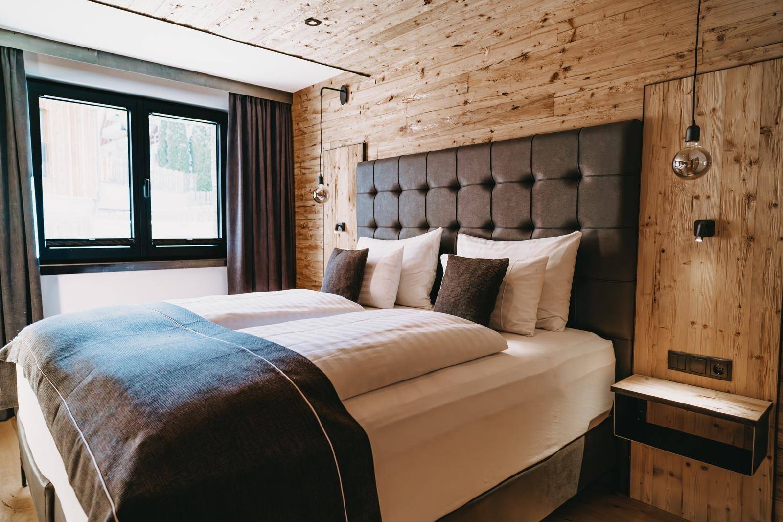 Komfortables Doppelbett mit gepolstertem Kopfteil und Holzwänden in einem hellen Schlafzimmer.