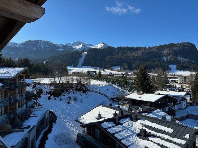 Weitläufiger Blick auf eine verschneite Berglandschaft mit Häusern und Skipisten.