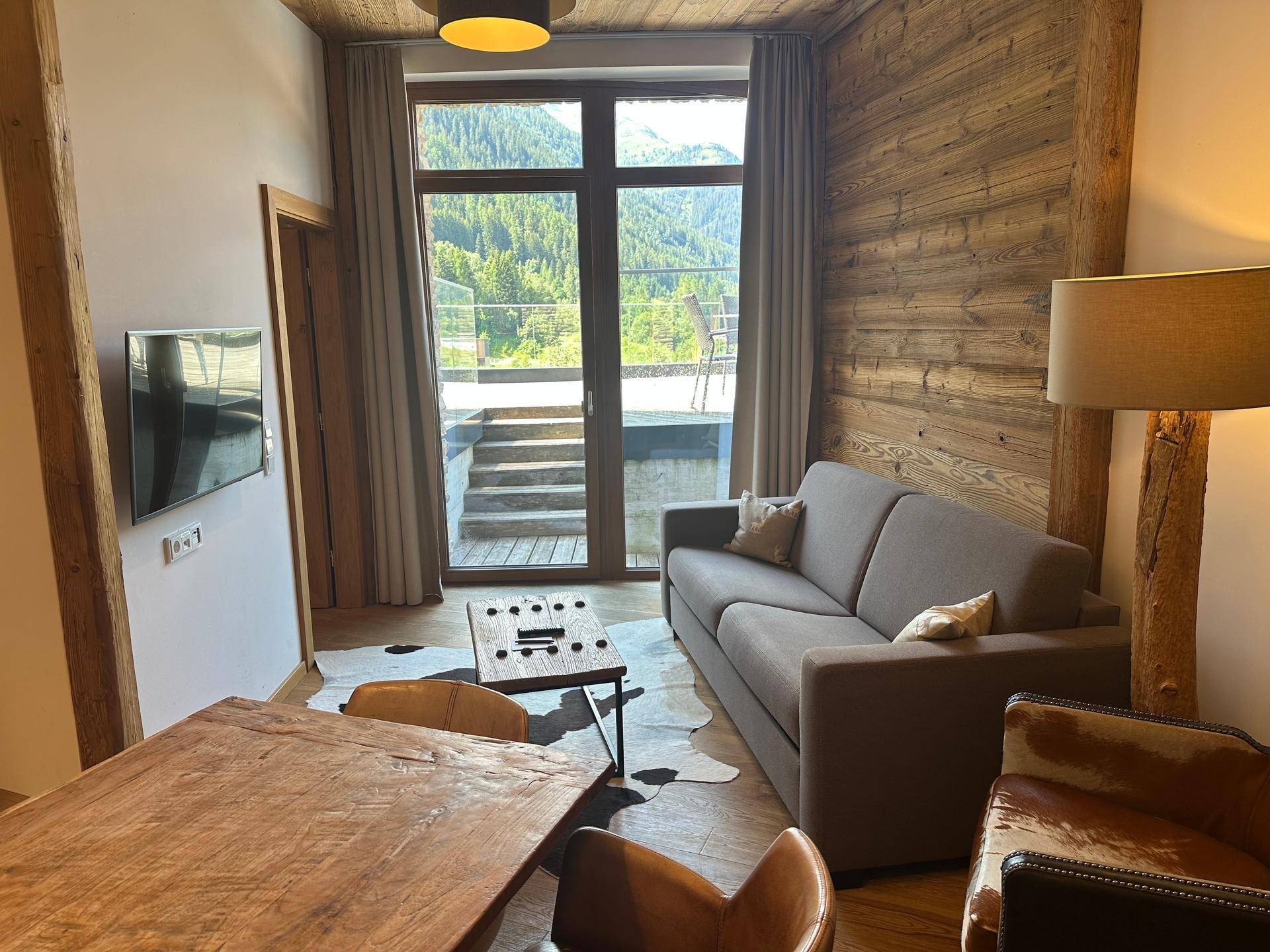 Helles Wohnzimmer mit bequemer Couch, Holztisch und großen Fenstern mit Bergblick.