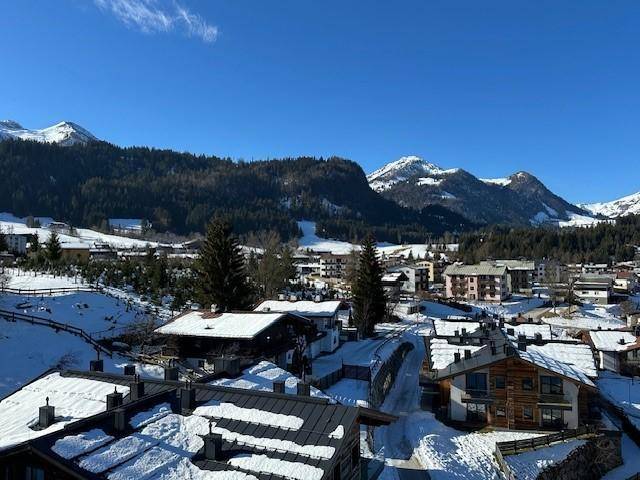 Panoramablick auf eine verschneite Berglandschaft mit traditionellen Häusern unter blauem Himmel.