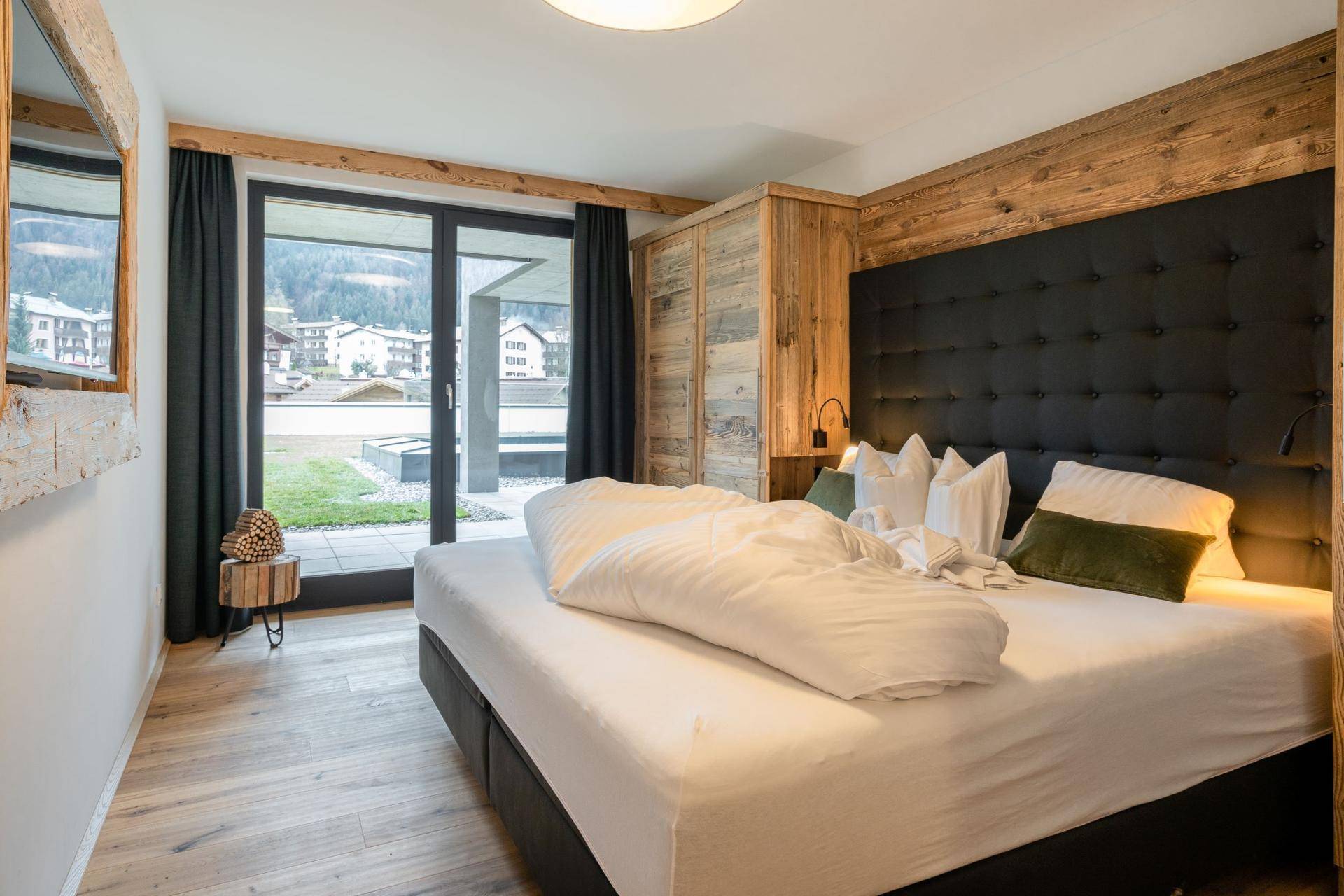 Helles Schlafzimmer mit großem Bett, Holzwand und Zugang zu einem kleinen Balkon.