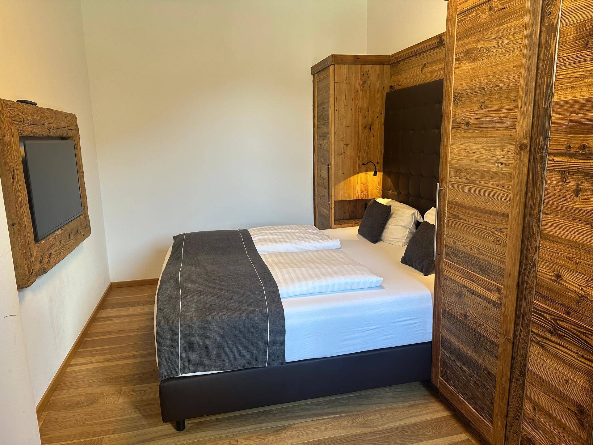 Helles Schlafzimmer mit Doppelbett, Holzschränken und einem an der Wand montierten Fernseher.