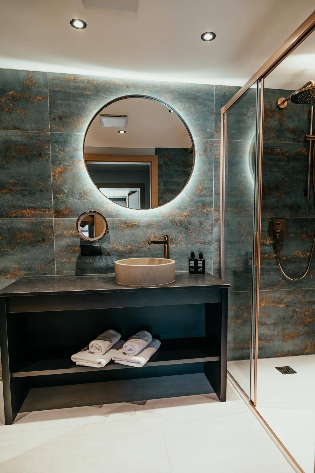 Modernes Badezimmer mit runden Spiegeln, begehbarer Dusche und stilvollen Fliesen in dunklen Tönen.