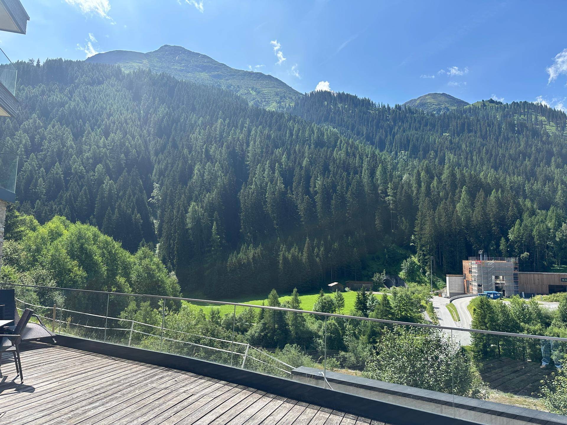 Sonniger Terrassenbereich mit Holzboden und weitem Blick auf die bewaldeten Berge und das Tal.