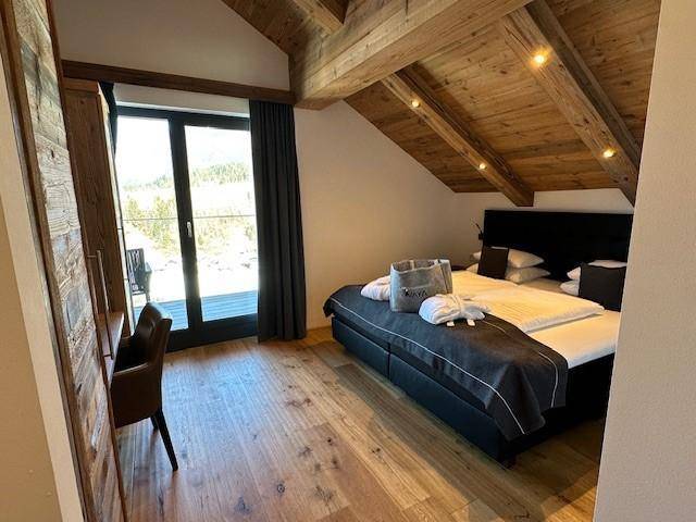 Gemütliches Schlafzimmer mit Doppelbett, Holzbalkendecke und Balkonzugang mit Bergblick.