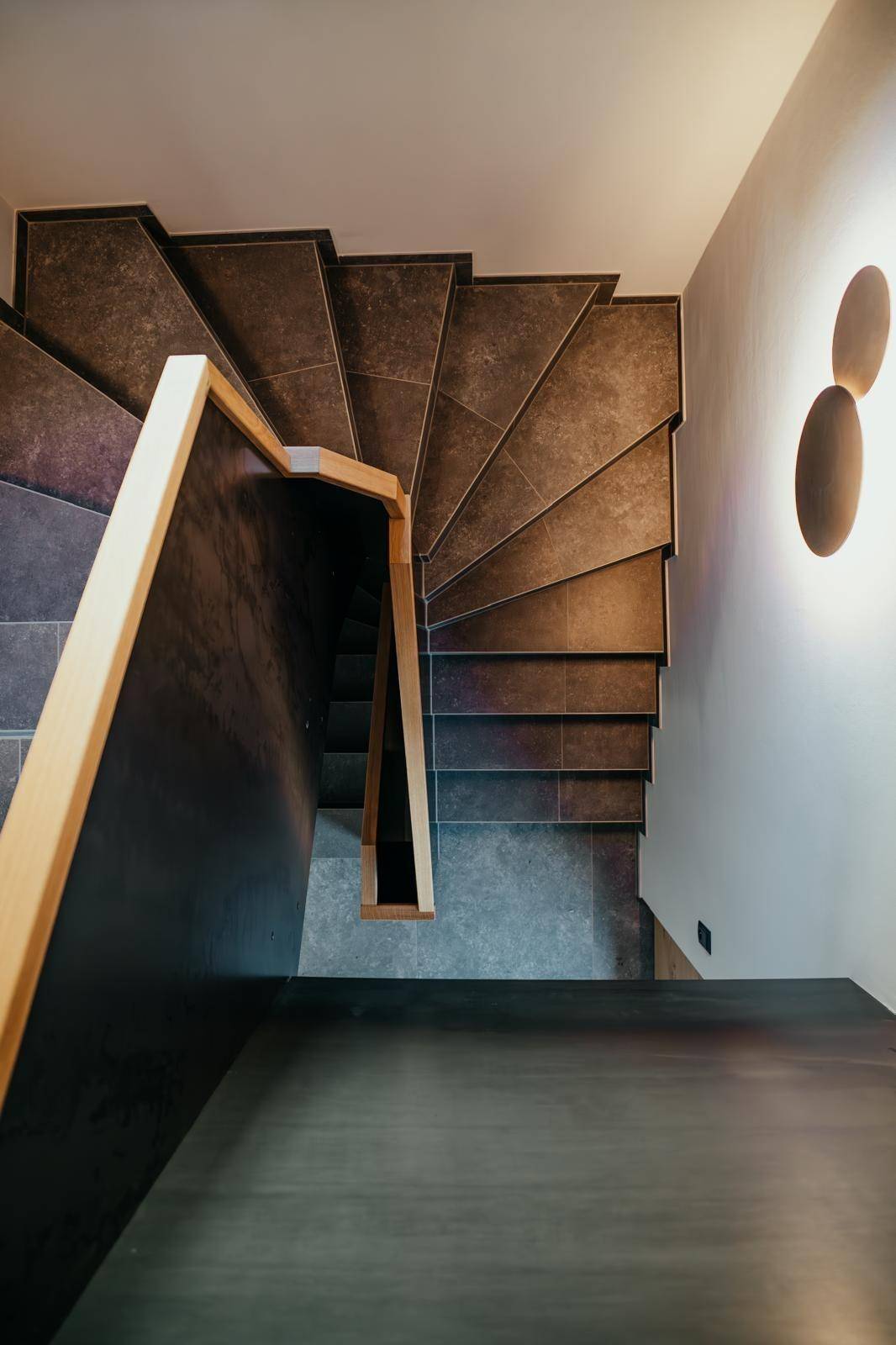 Moderne Treppe mit Fliesenstufen und Holzgeländer, die verschiedene Ebenen verbindet.