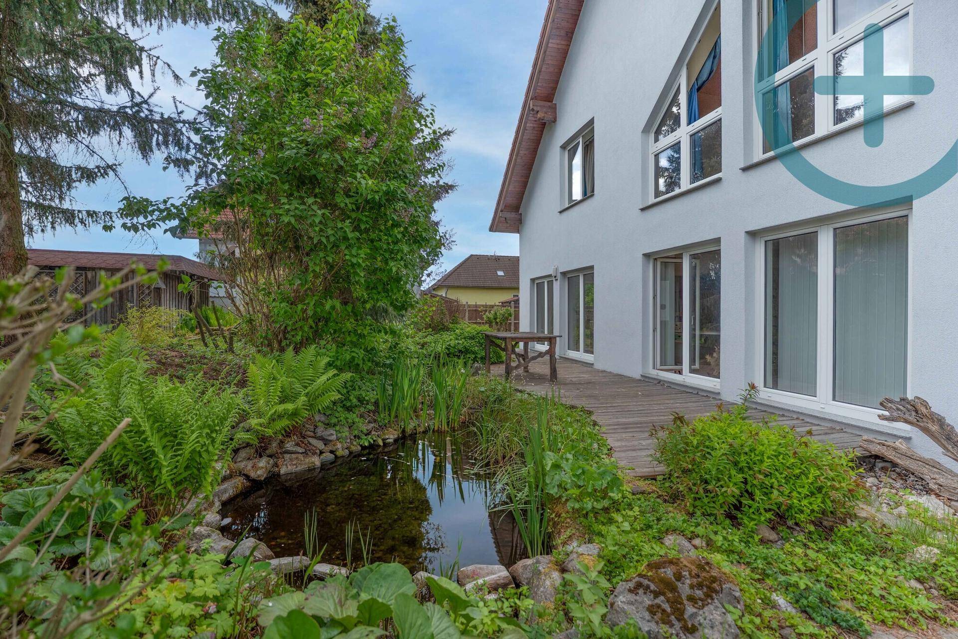 Idyllischer Gartenteich mit Holzterrasse und üppiger Bepflanzung neben dem Haus.