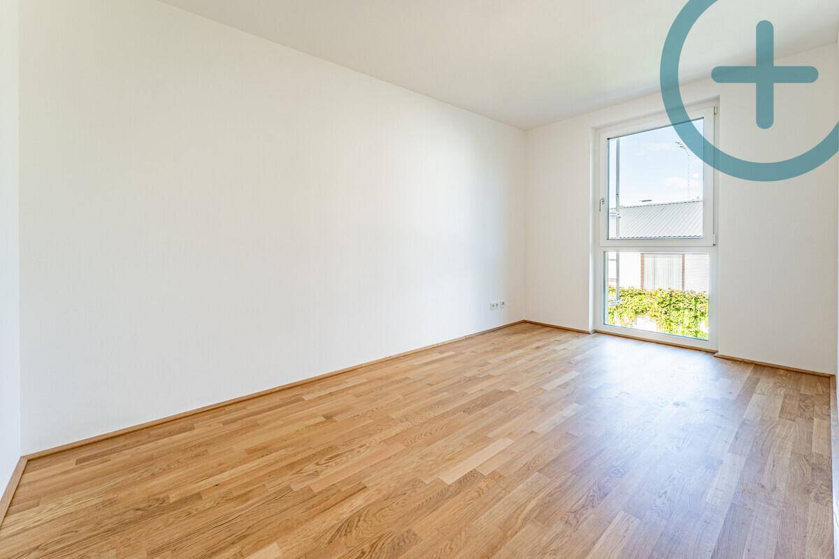 Helles Schlafzimmer mit Parkettboden und großem Fenster mit Blick ins Grüne.