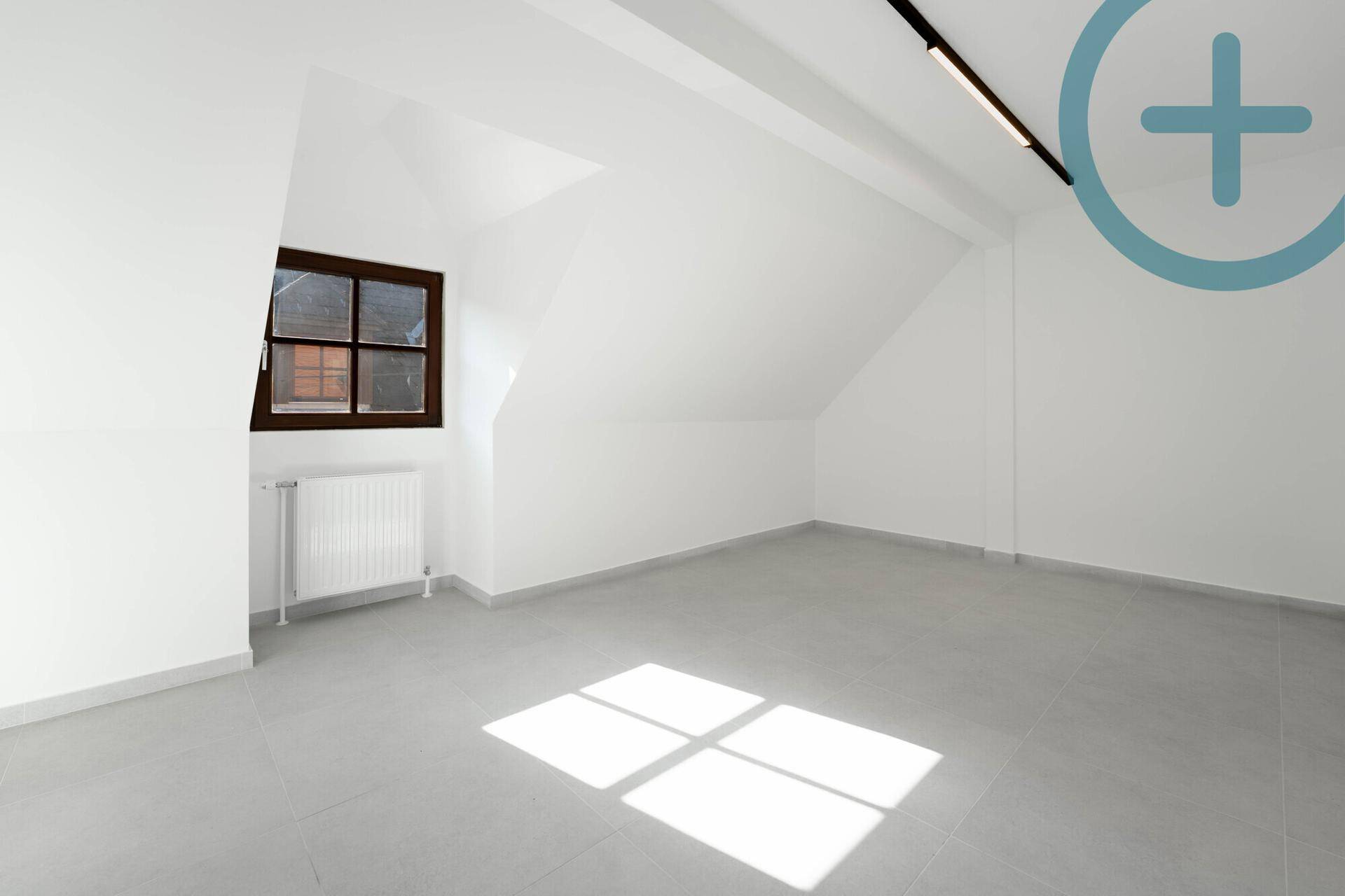 Leerer Raum mit Fliesenboden, weiß gestrichenen Wänden und einem Fenster, das Sonnenlicht hereinlässt.