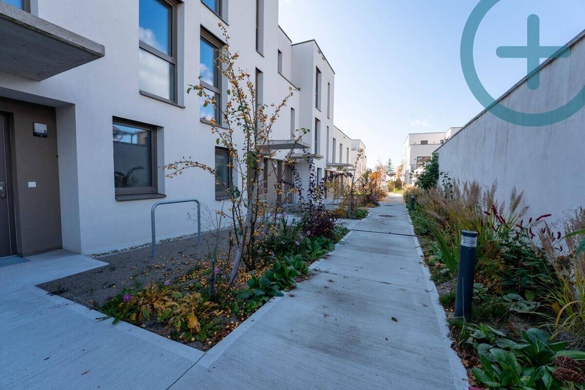Fußweg zwischen modernen Gebäuden mit gepflegten Grünflächen und Bepflanzung.