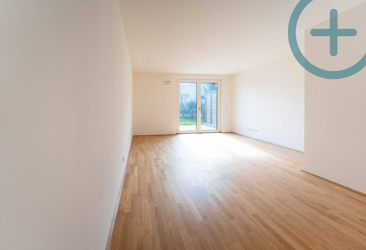 Heller, leerer Wohnraum mit Parkettboden und Schiebetür zum privaten Gartenbereich.
