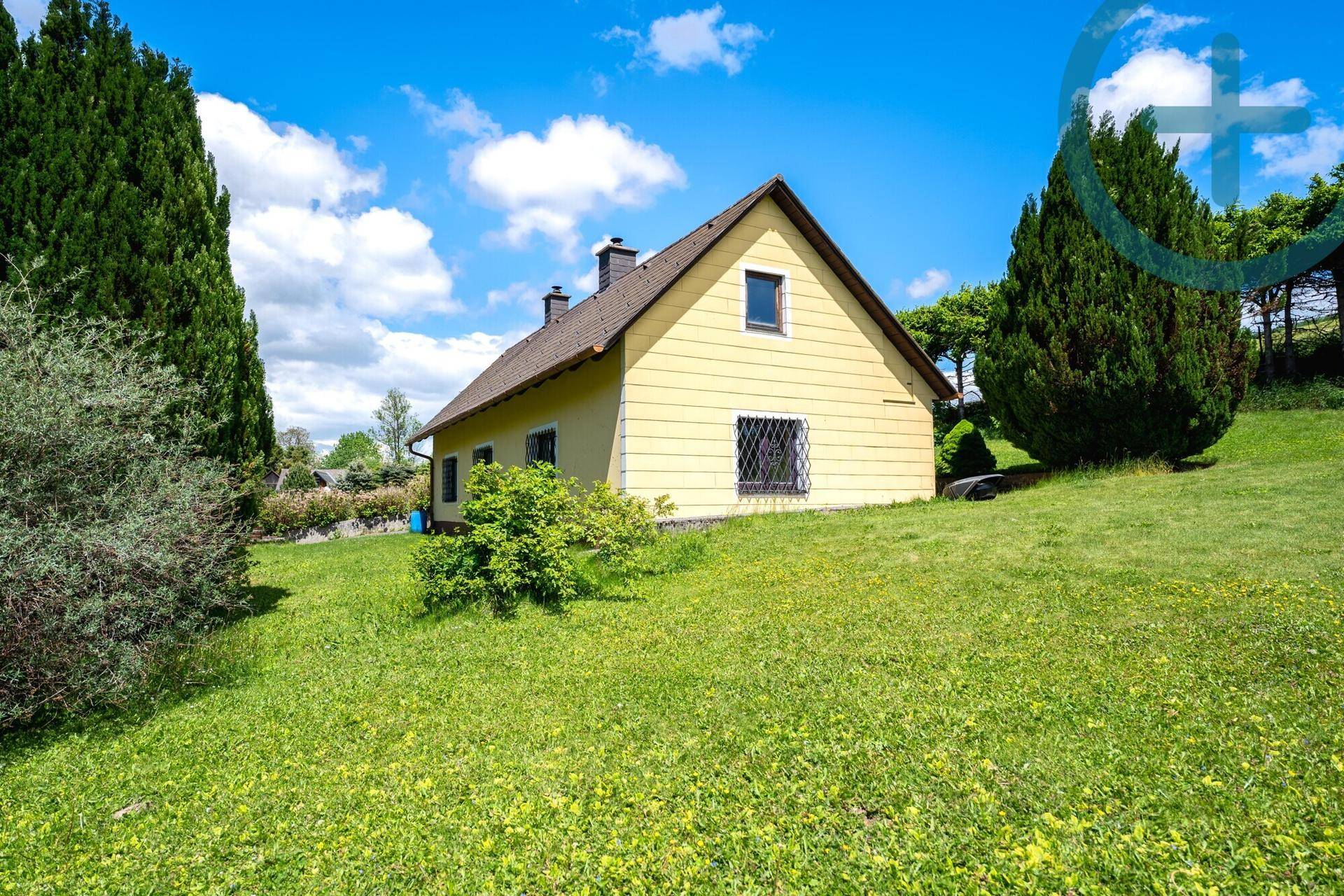 Weitläufiger Garten mit grünem Rasen und dem gelben Haus unter blauem Himmel.