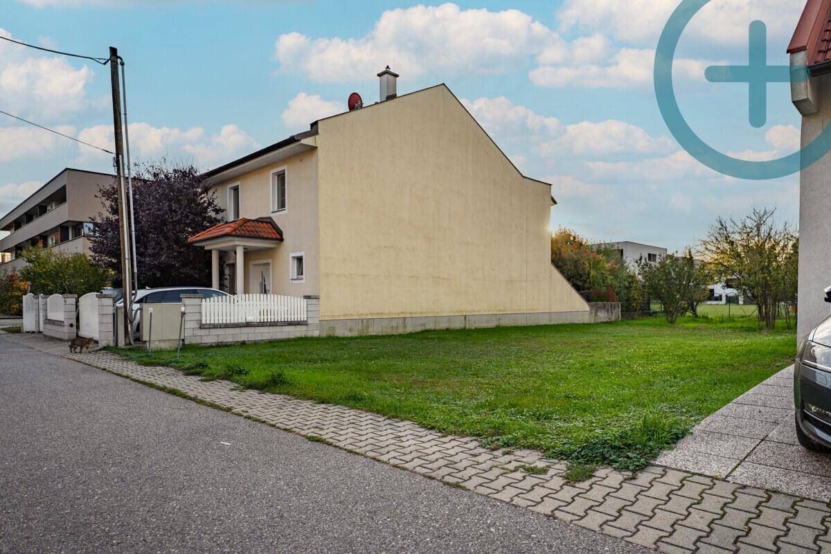 Seitenansicht eines Wohnhauses neben einer freien Rasenfläche mit angrenzender Straße.