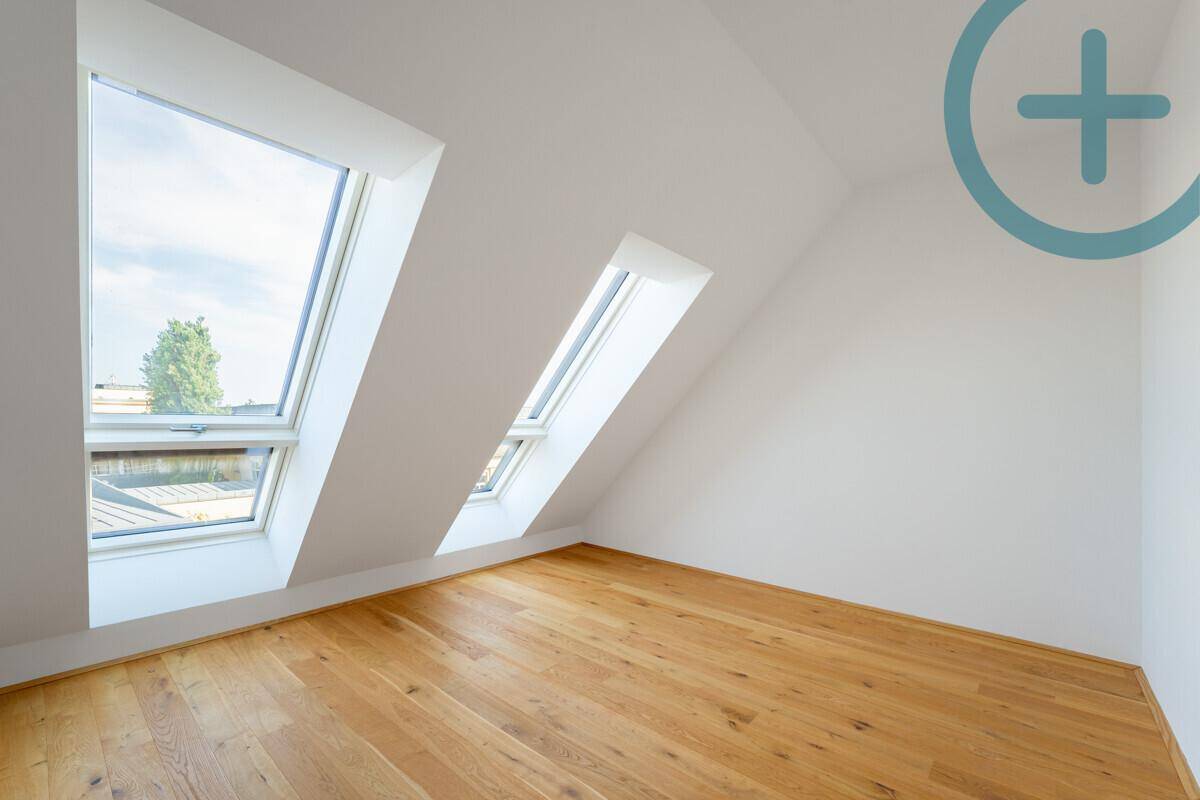 Helles Dachzimmer mit Holzboden und zwei schrägen Dachfenstern, ideal als Schlafzimmer.