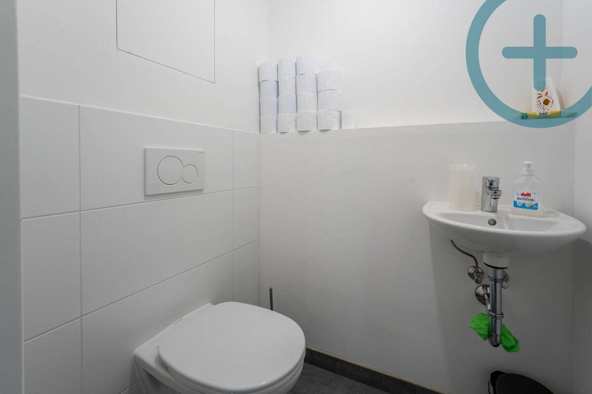 Kleines Gäste-WC mit wandhängender Toilette, kleinem Waschbecken und weißen Fliesen.