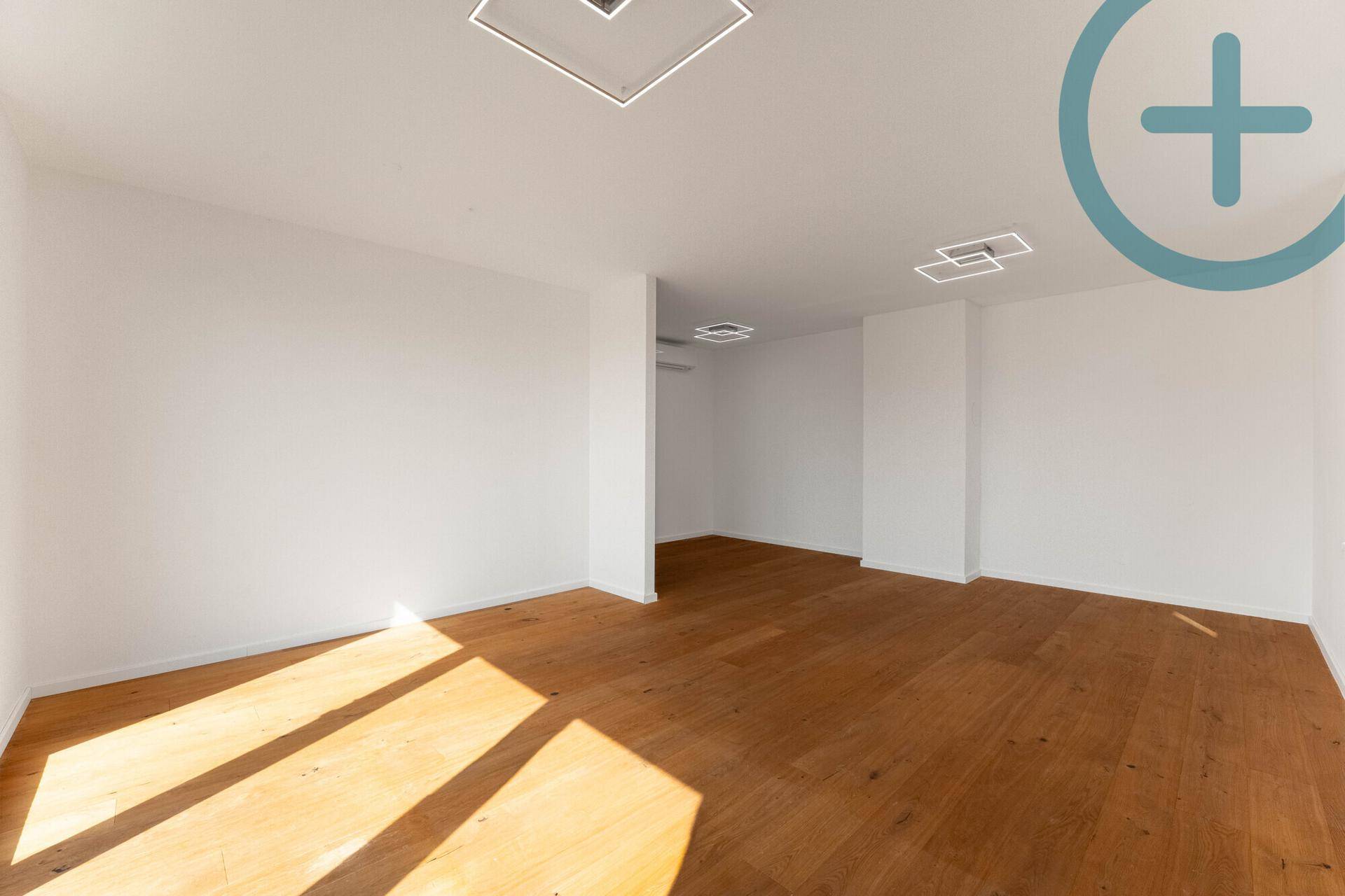 Lichtdurchfluteter Raum mit elegantem Holzplankenboden und minimalistischen Deckenleuchten.