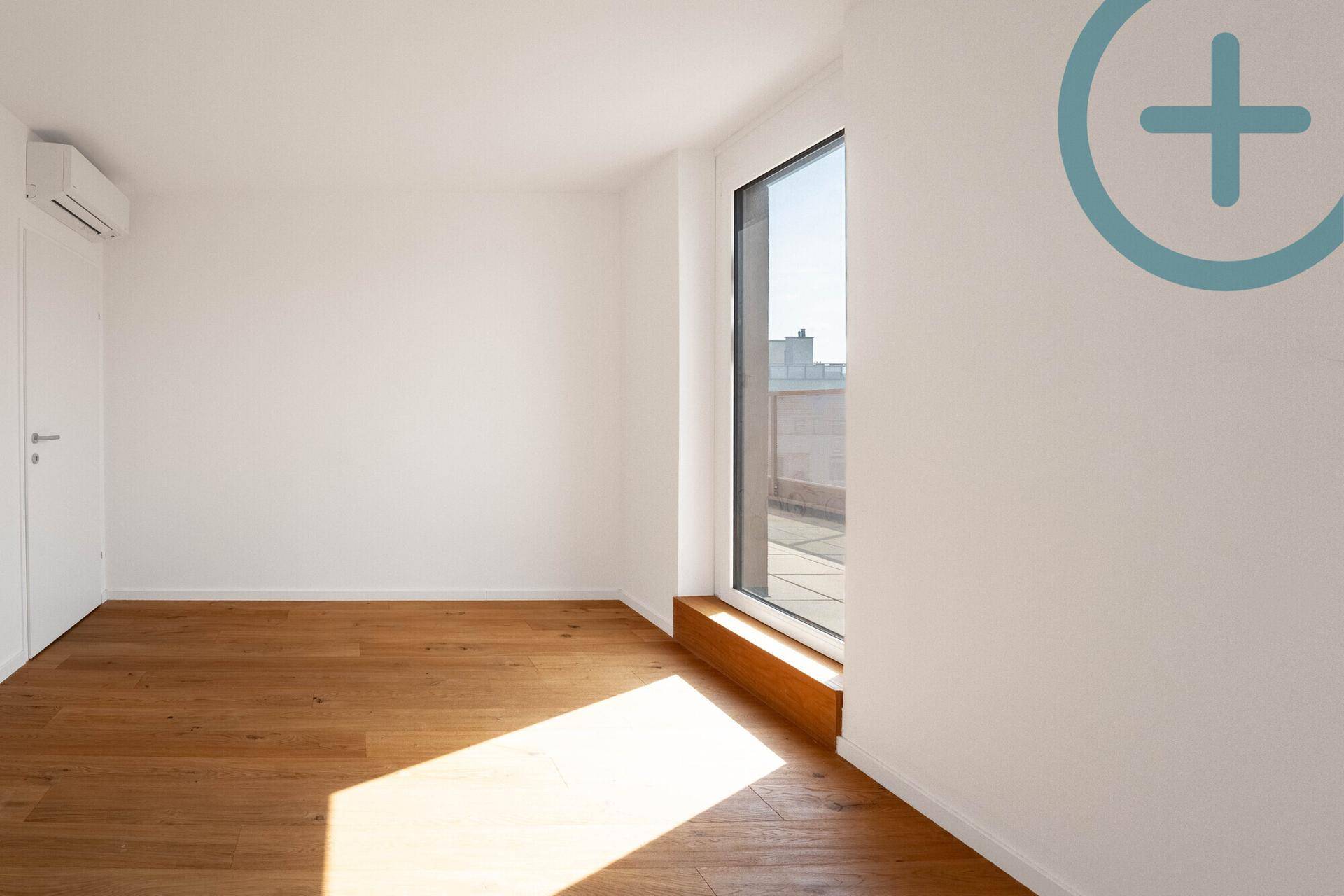 Lichtdurchflutetes Zimmer mit Holzplankenboden, bodentiefem Fenster und Klimaanlage.